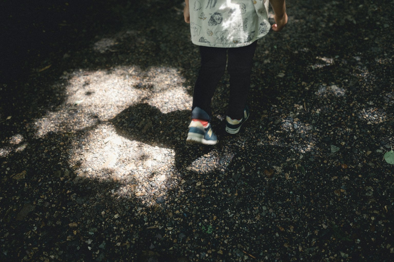 Pies de un niño caminando en sombras un zapato es azul con un diseño colorido