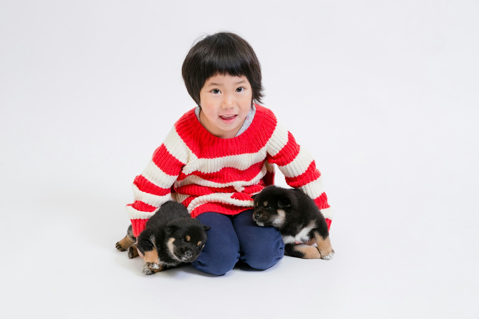 Anak dengan sweater bergaris merah dan putih duduk bersama dua anak anjing