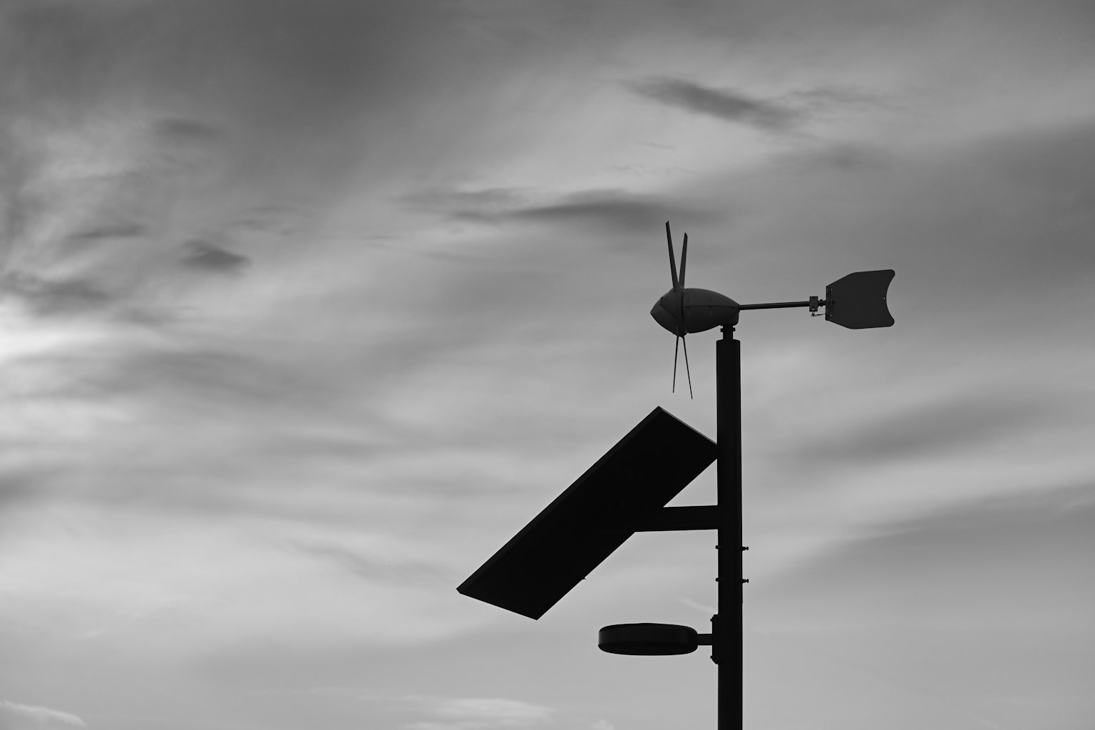 Silhouette eines Masts mit einer Windturbine und einem Solarpanel