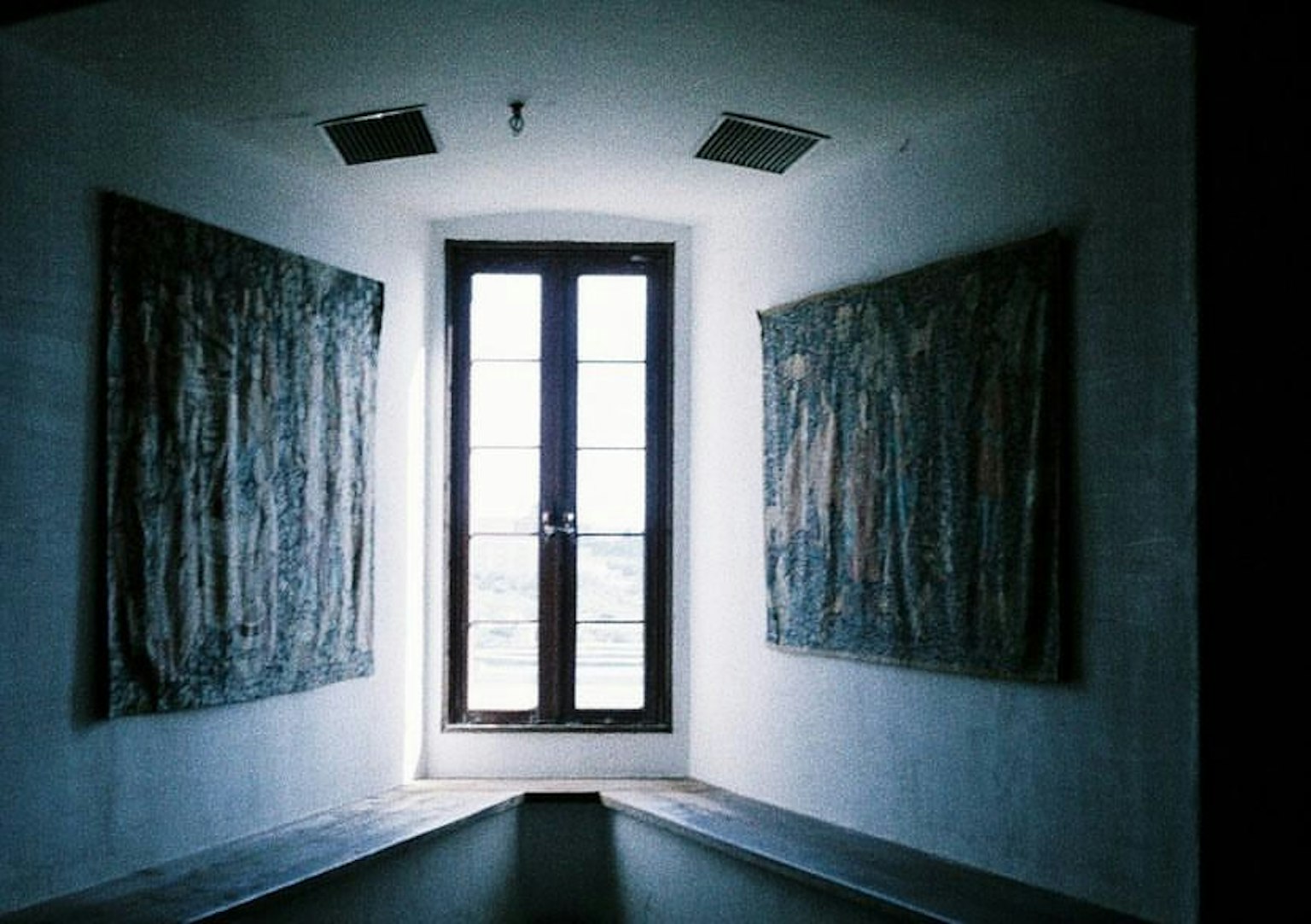 Brightly lit hallway with a window and tapestries on the walls