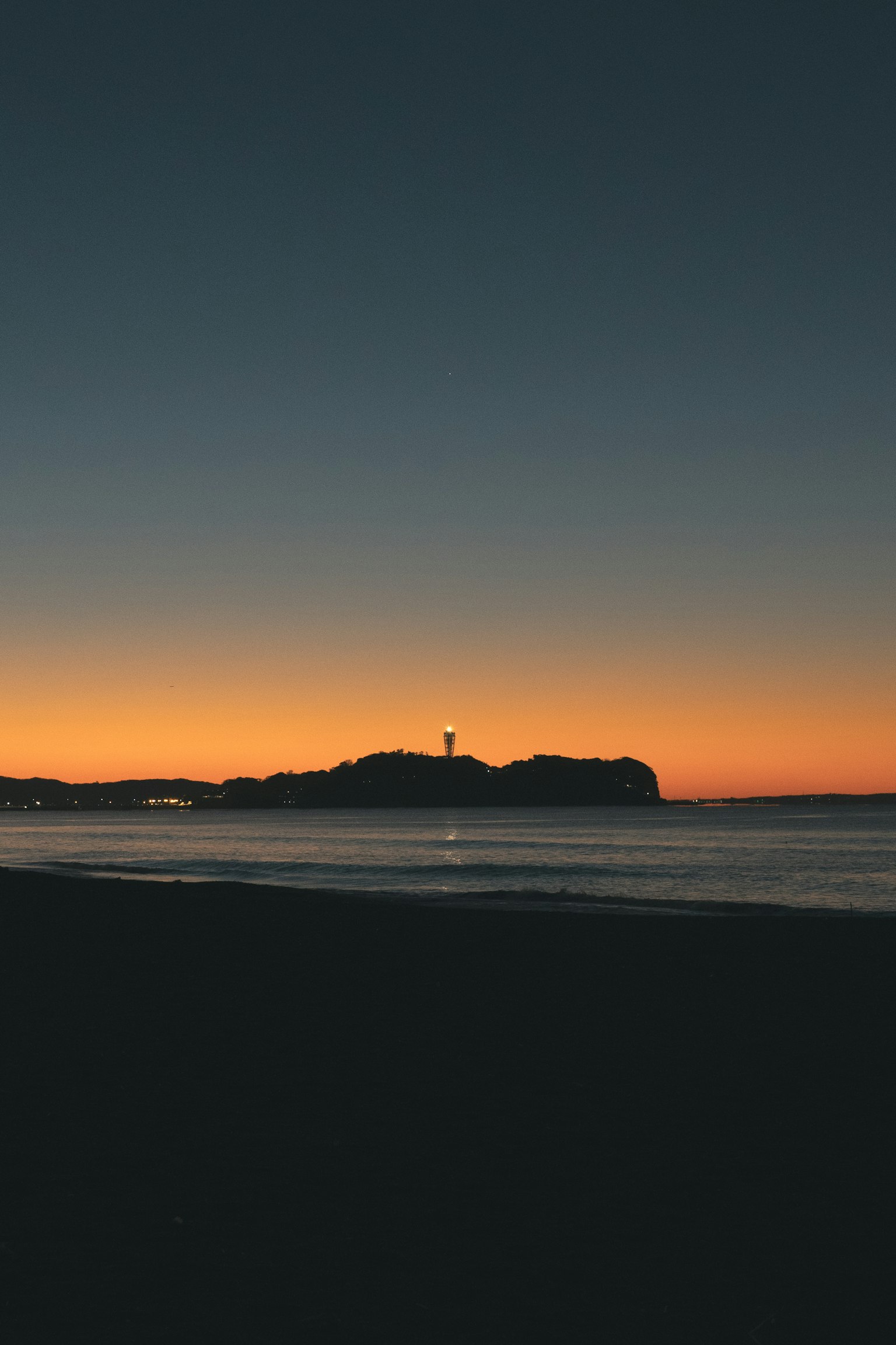 Insel mit einem Leuchtturm gegen einen Sonnenuntergangshimmel silhouettiert