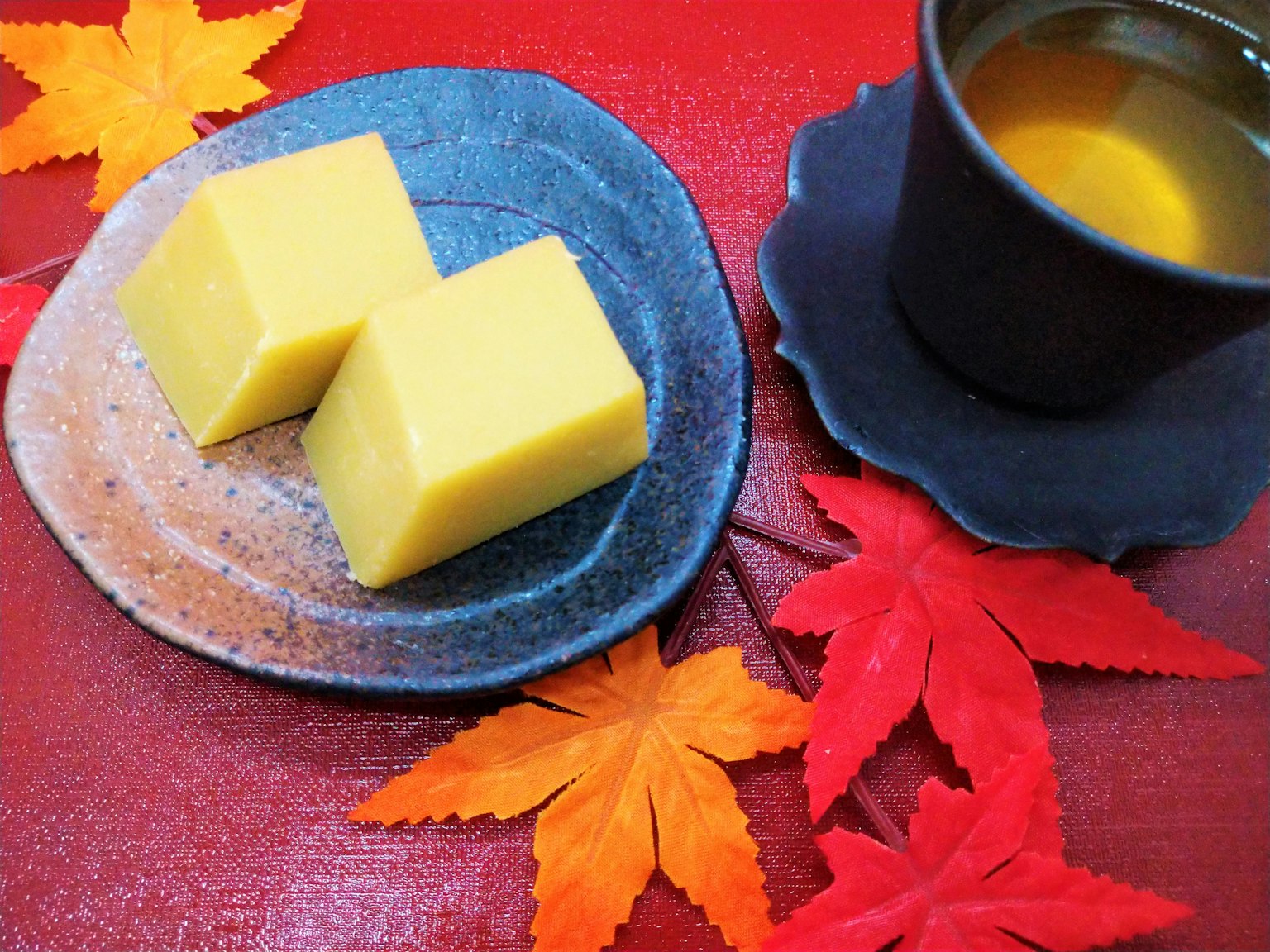 Kue Jepang kuning di atas piring dengan daun musim gugur dan secangkir teh