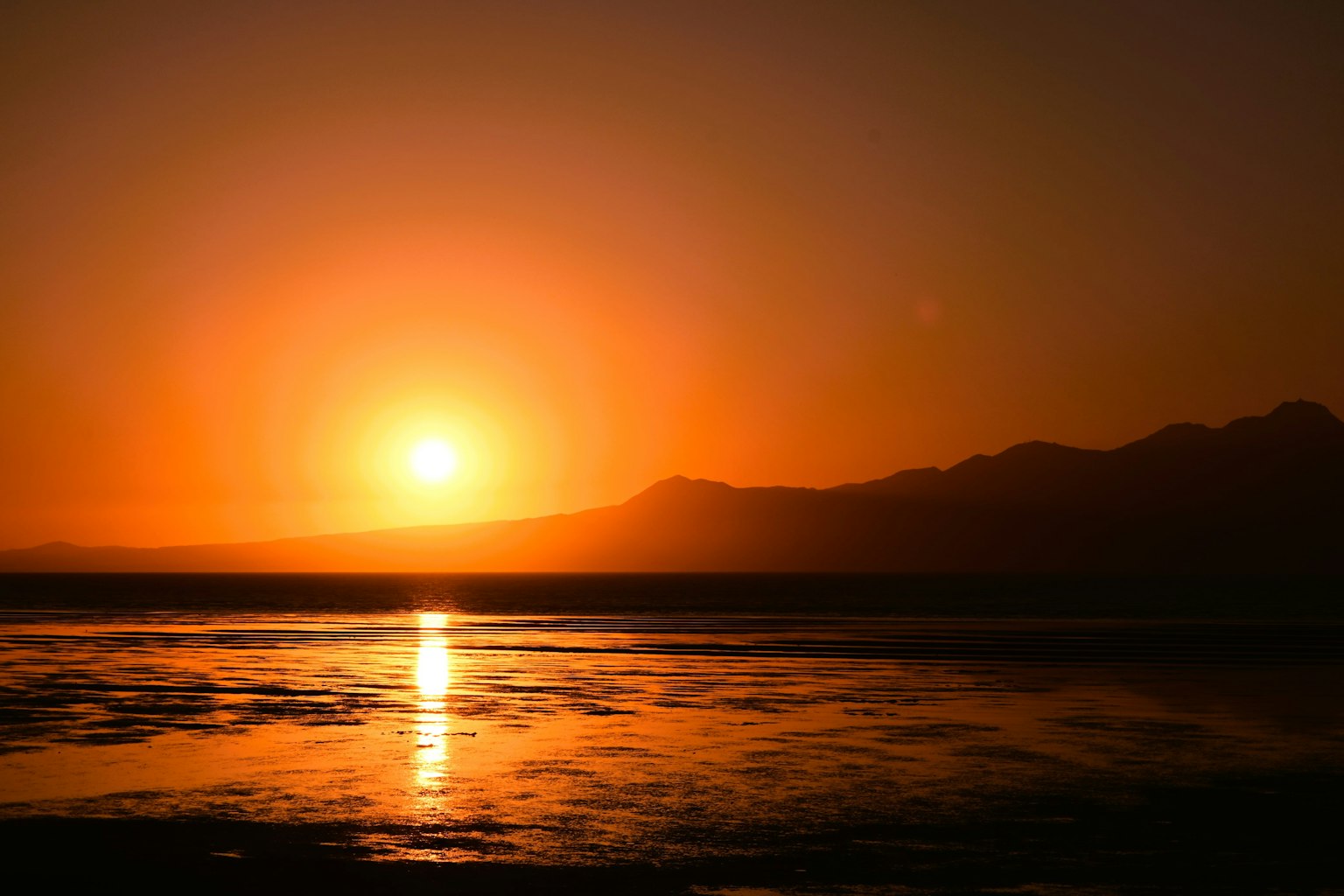 Stupendo tramonto arancione dietro le montagne che si riflette nell'acqua