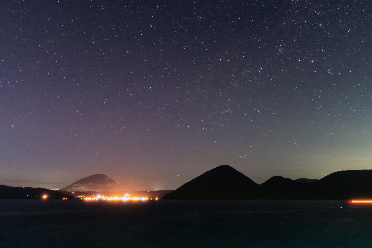 Vista panoramica di montagne sotto un cielo stellato con luci lontane