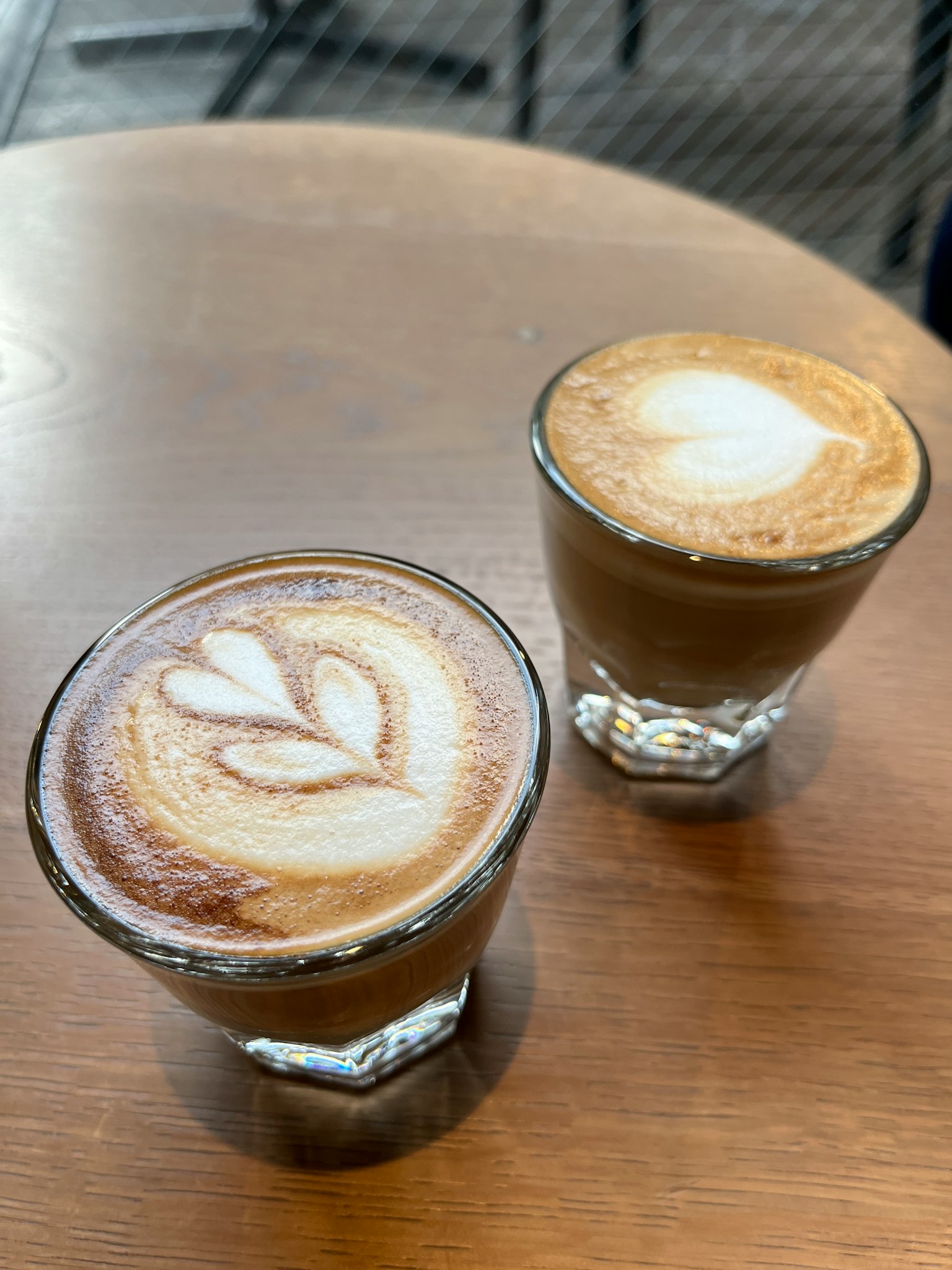 Dua cangkir kaca cappuccino dan latte art di atas meja kayu