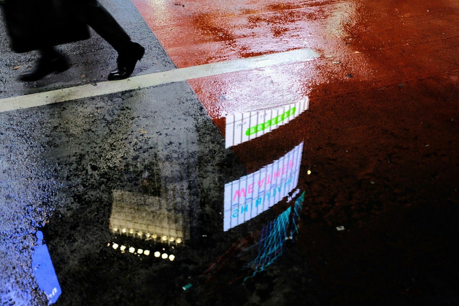 Phản chiếu của đèn neon trên vỉa hè ướt với dấu chân của một người