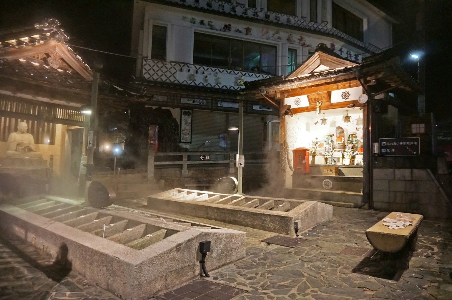 Night view of a hot spring town featuring traditional buildings and a steaming onsen