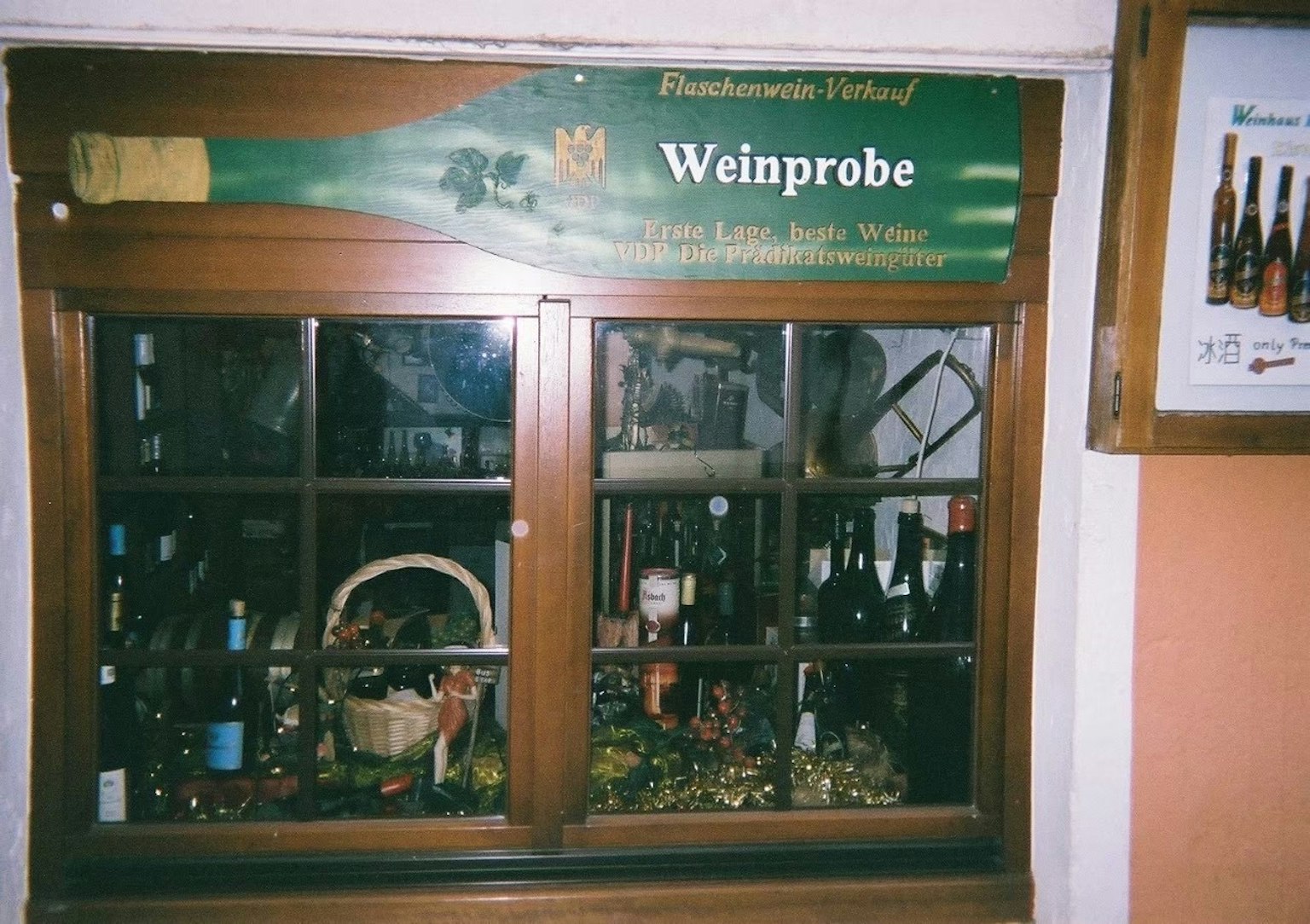 Wooden window displaying wine bottles and decorative items with a sign saying Weinprobe
