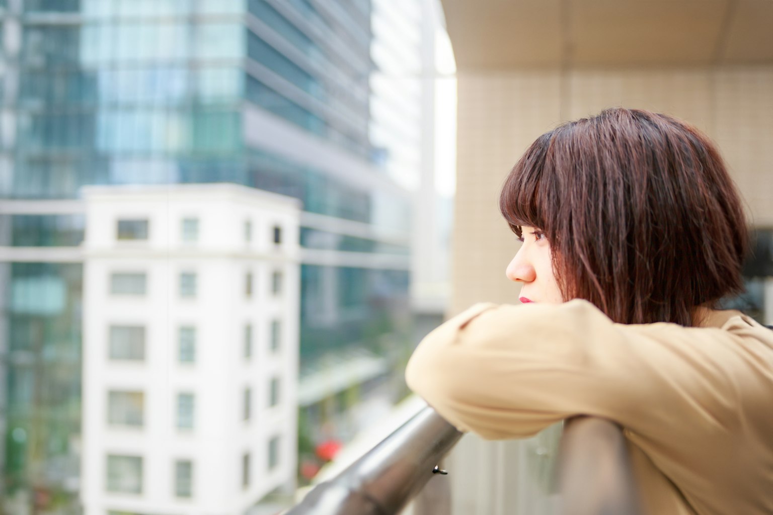 Một người phụ nữ nhìn ra ngoài từ ban công với các tòa nhà chọc trời ở phía sau
