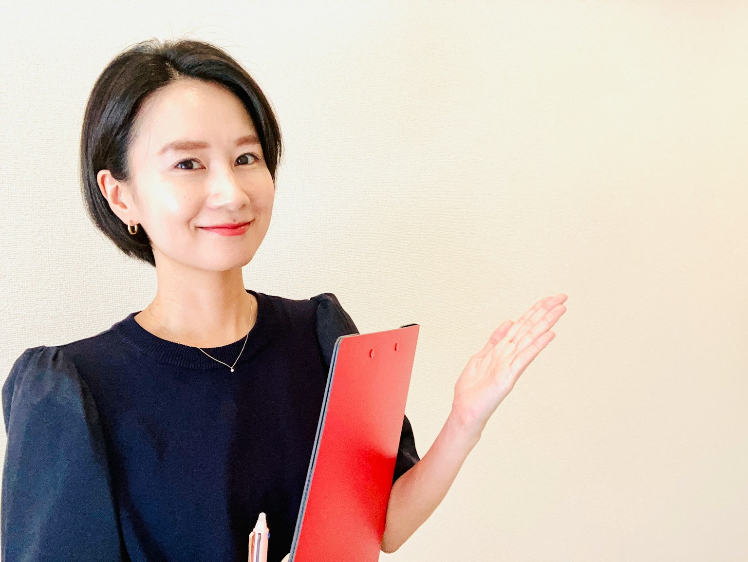 Seorang wanita berpakaian kasual bisnis memegang clipboard merah dan tersenyum
