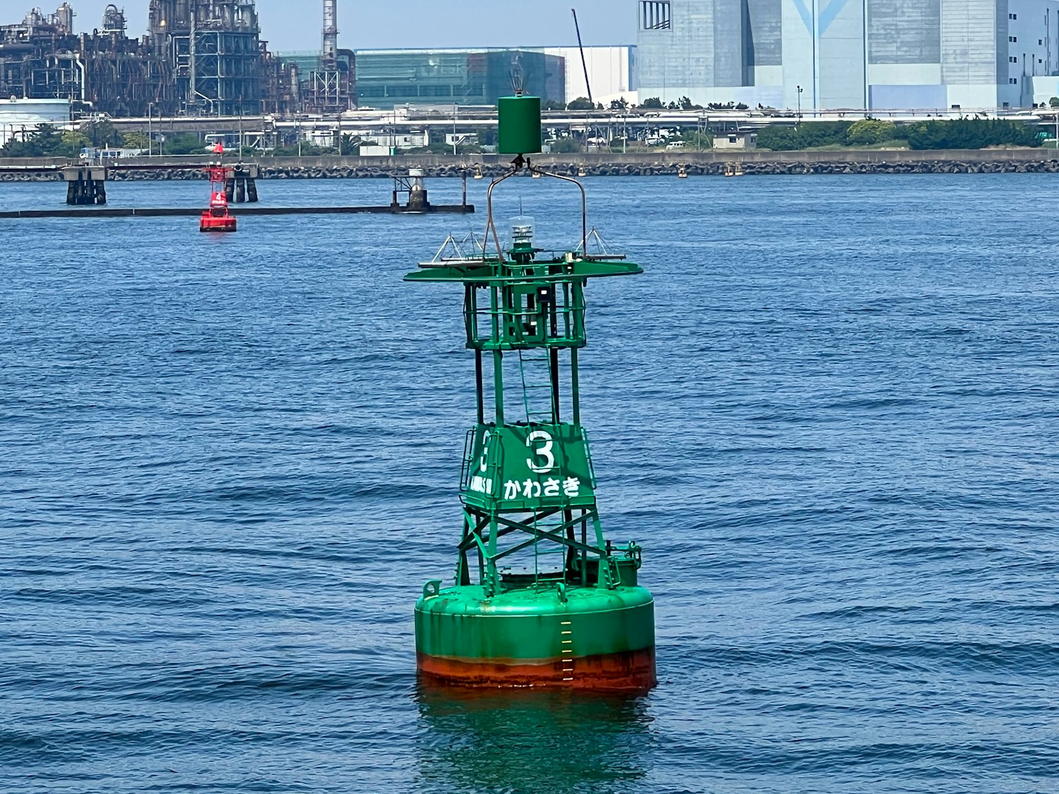 Boyas verdes flotando en el agua con fábricas y edificios al fondo