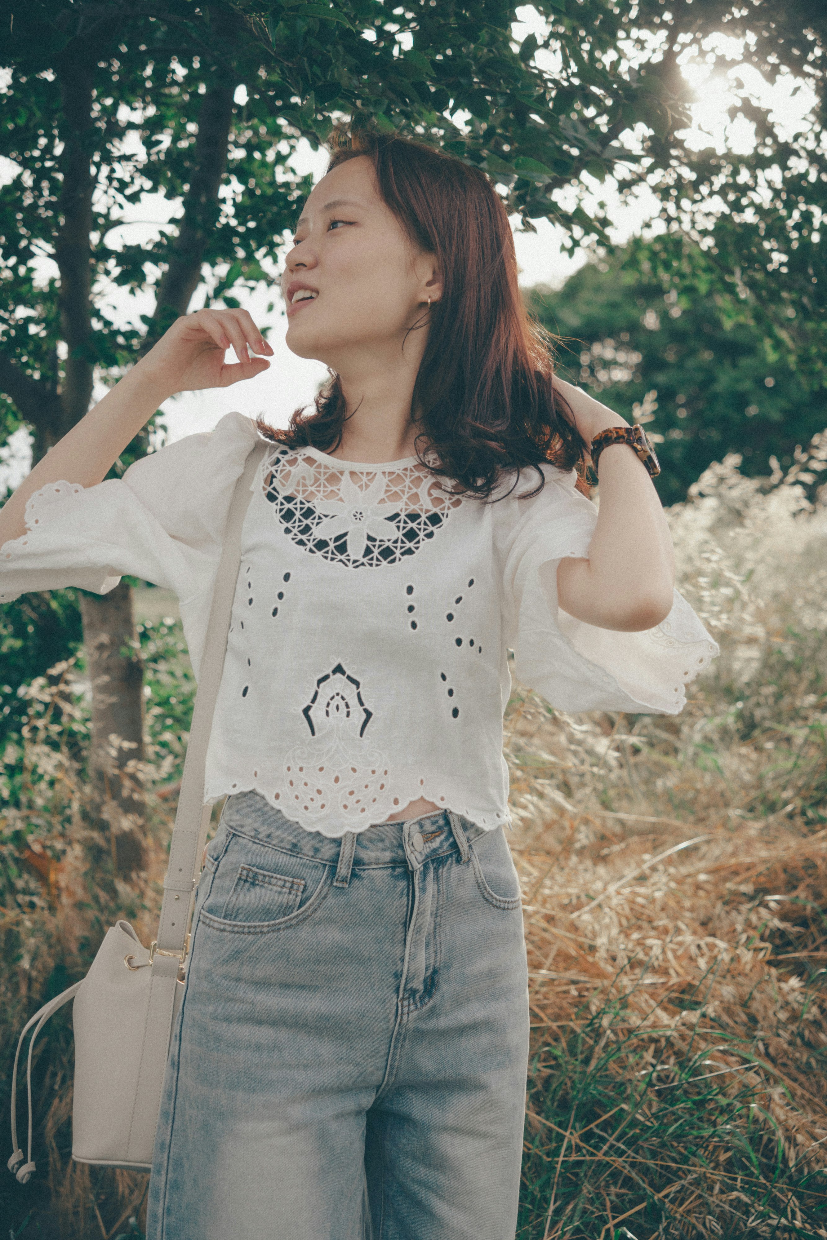 木立の中で微笑む女性の横顔と手に持つ小さな花束