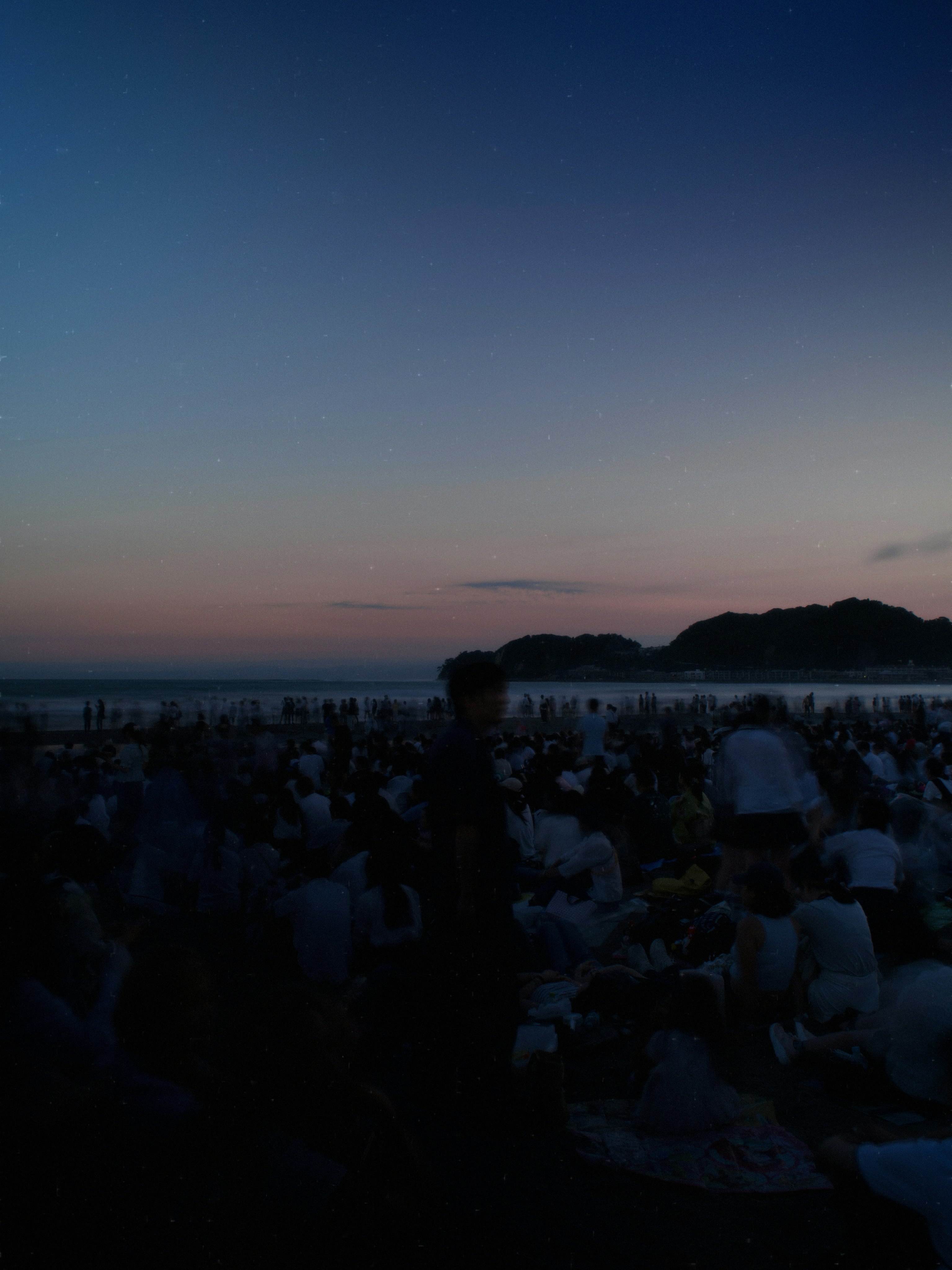 海辺の花火大会を見上げる夕暮れの観客