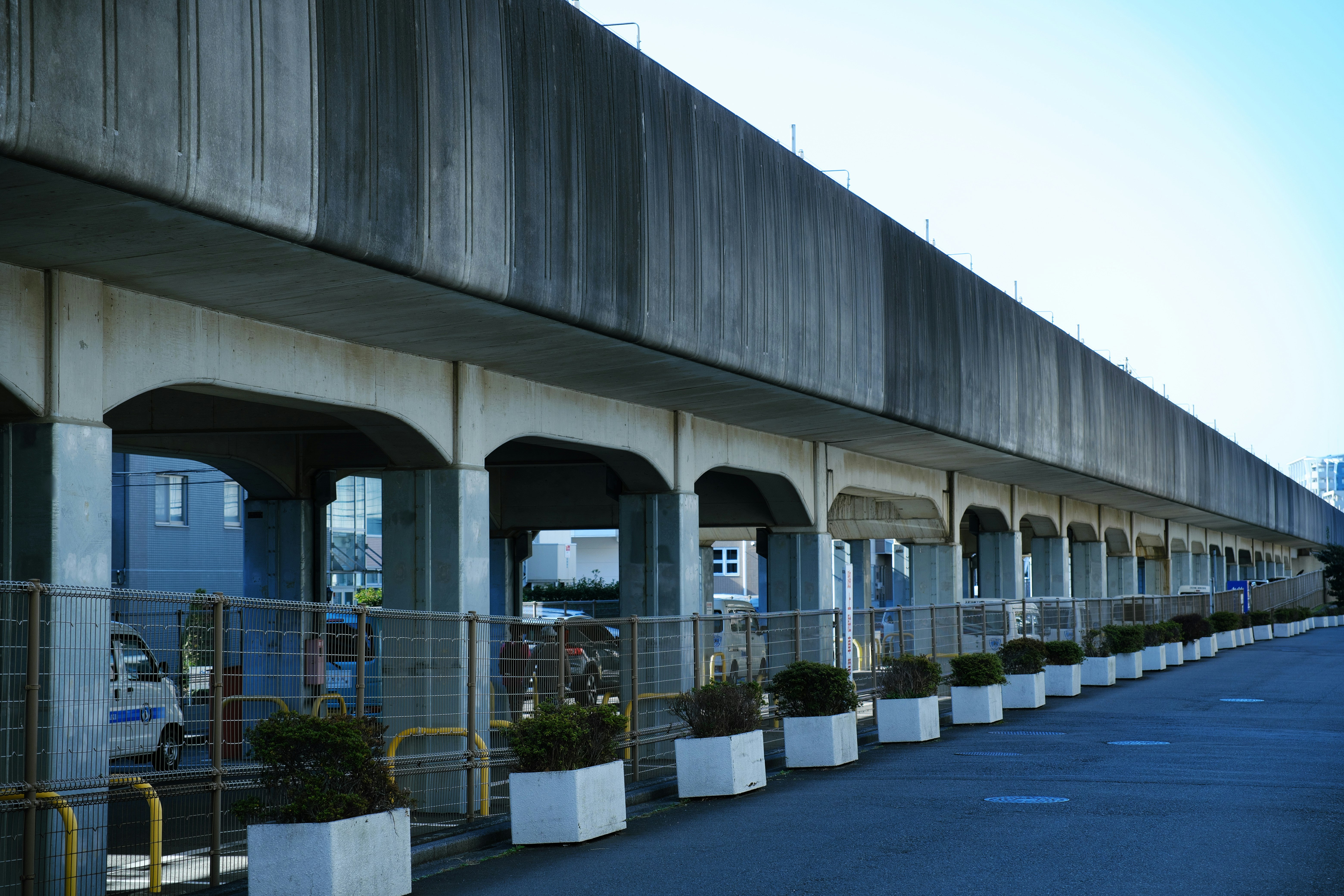 Hochbahnviadukt mit Bögen und Reihe von Pflanzkübeln entlang des Gehwegs