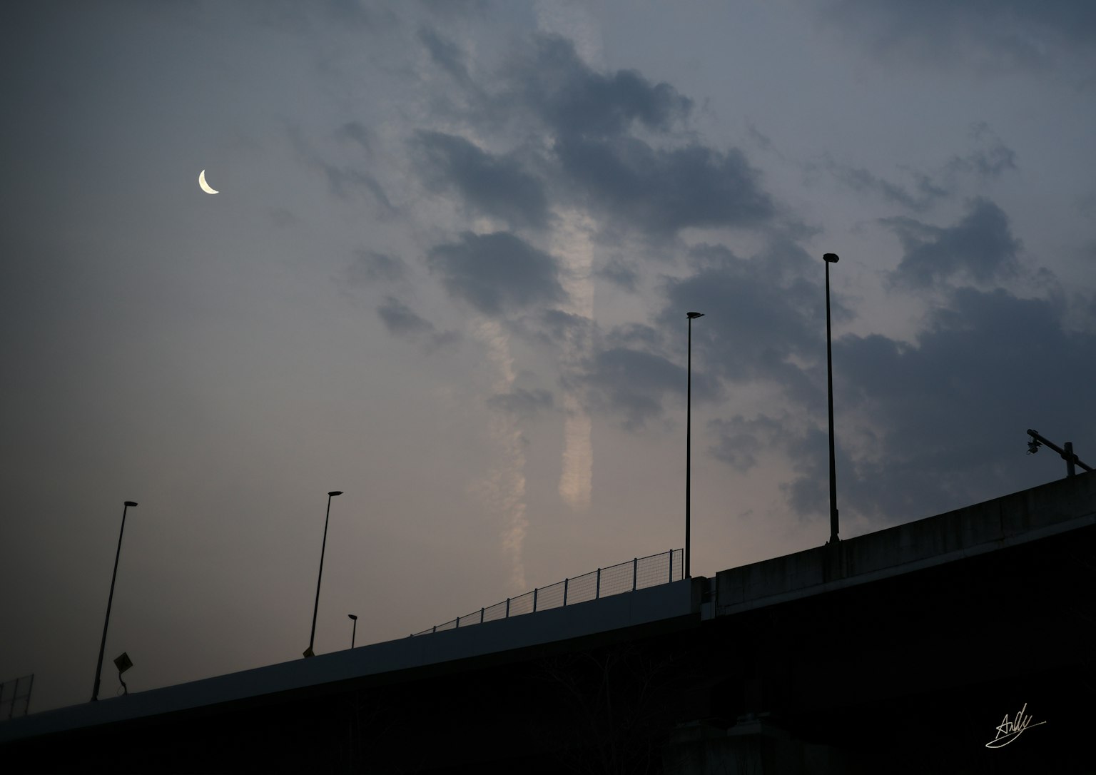 Silhouette di un ponte sotto una luna crescente e nuvole in un cielo dim