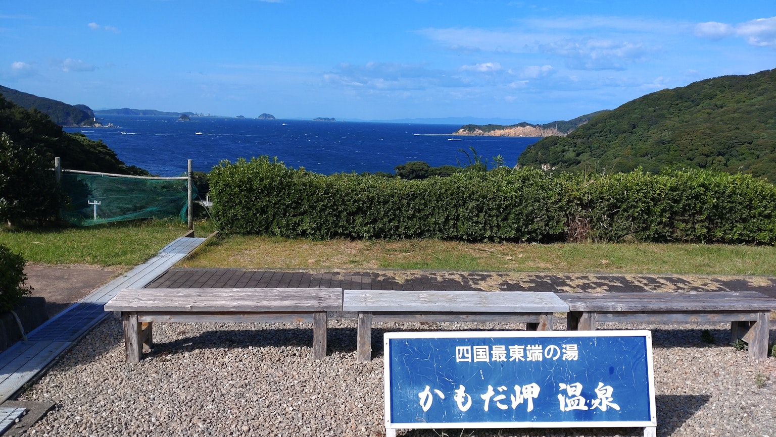 Vista escénica del océano azul y colinas verdes con el letrero de Kamoda Onsen