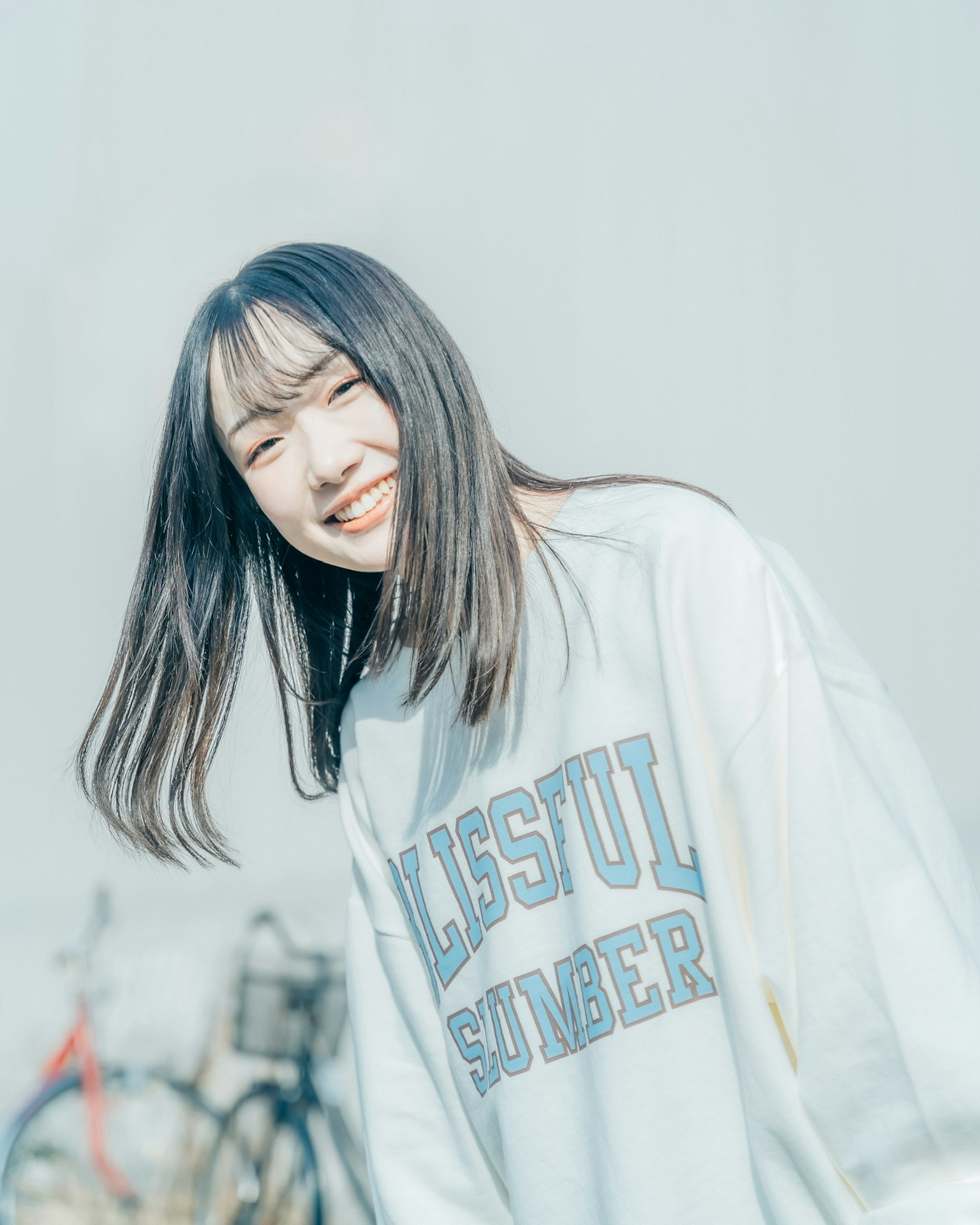 Junge Frau mit einem strahlenden Lächeln, die ein weißes Sweatshirt trägt, mit Fahrrädern im Hintergrund