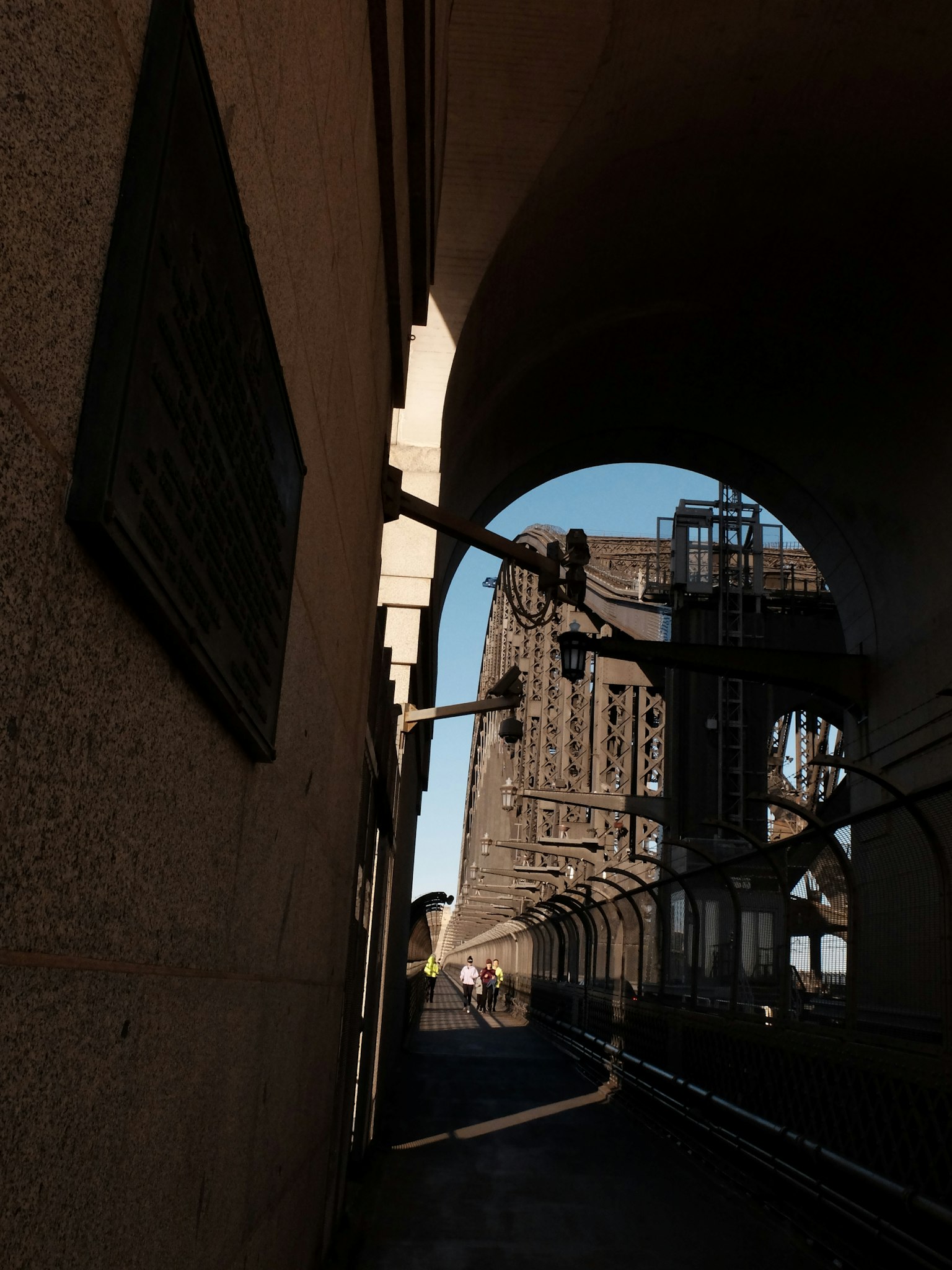 Photo of a walkway beneath an arch of a bridge showcasing surrounding structures