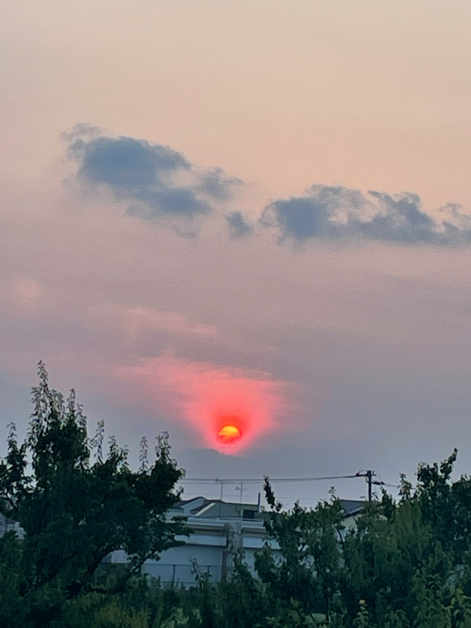 Sole rosso che tramonta in un cielo nebbioso con nuvole