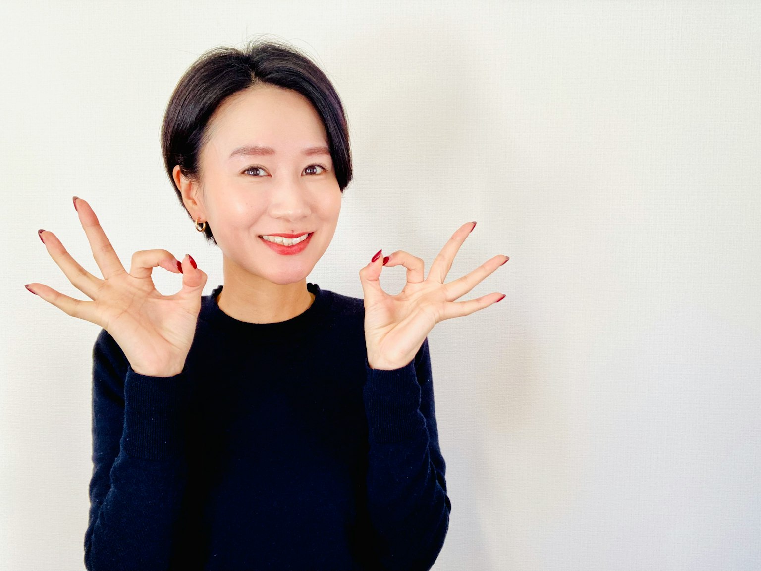 一位穿著黑色毛衣的女性在白色背景前微笑著舉著硬幣