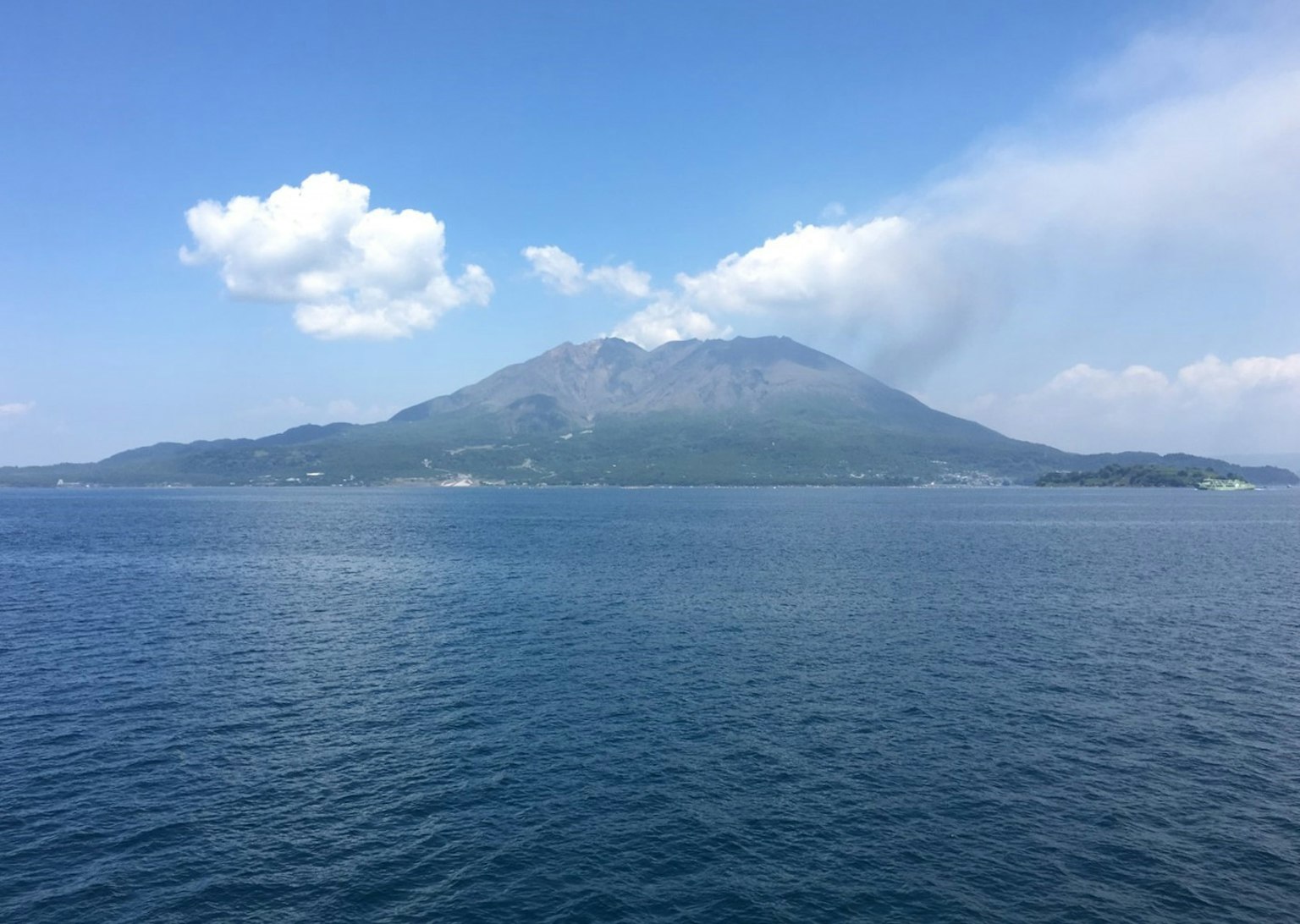 Une vue panoramique d'une montagne entourée par la mer bleue et des nuages