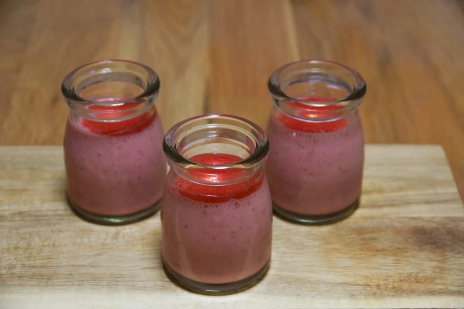 Trois petits pots en verre remplis de gelée rouge et de dessert rose