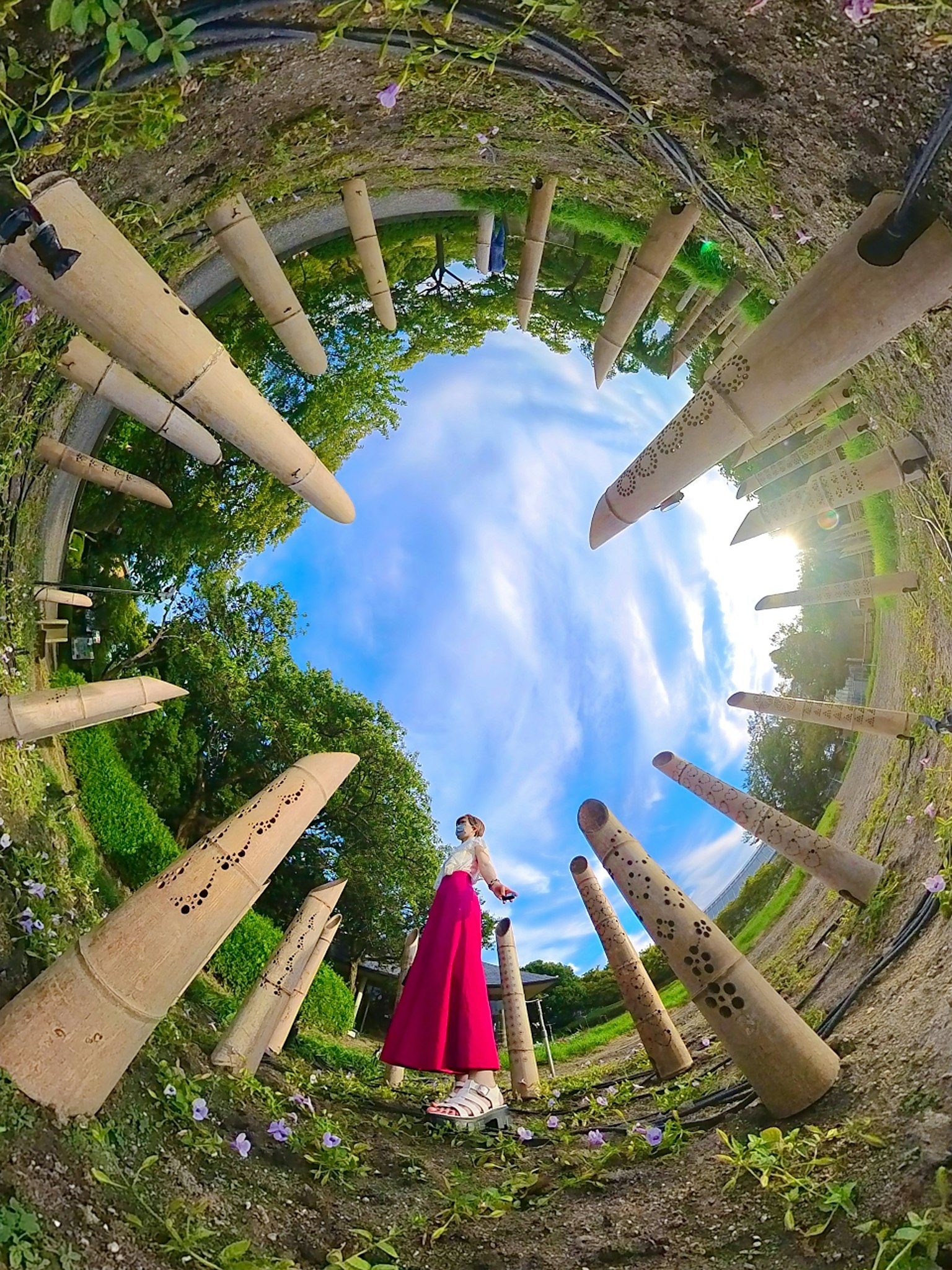 Une femme en robe rouge se tient parmi des objets circulaires sous un ciel bleu entouré d'herbe verte