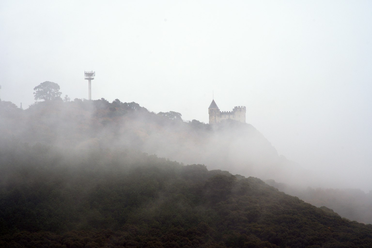 Bâtiment ancien et tour de communication enveloppés de brouillard sur une colline