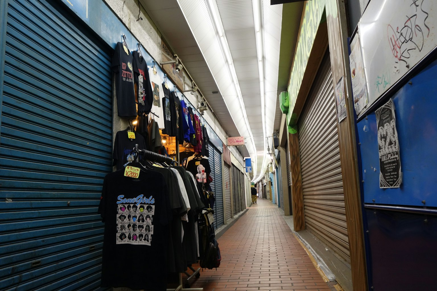 Pasillo estrecho con ropa colgada y persianas cerradas en un centro comercial
