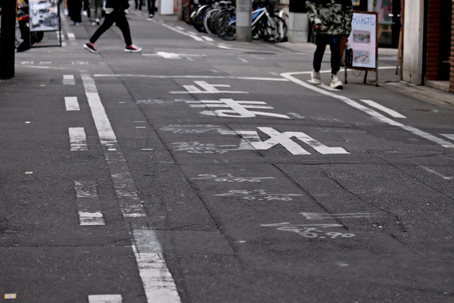 A narrow street with pedestrians walking and road markings visible