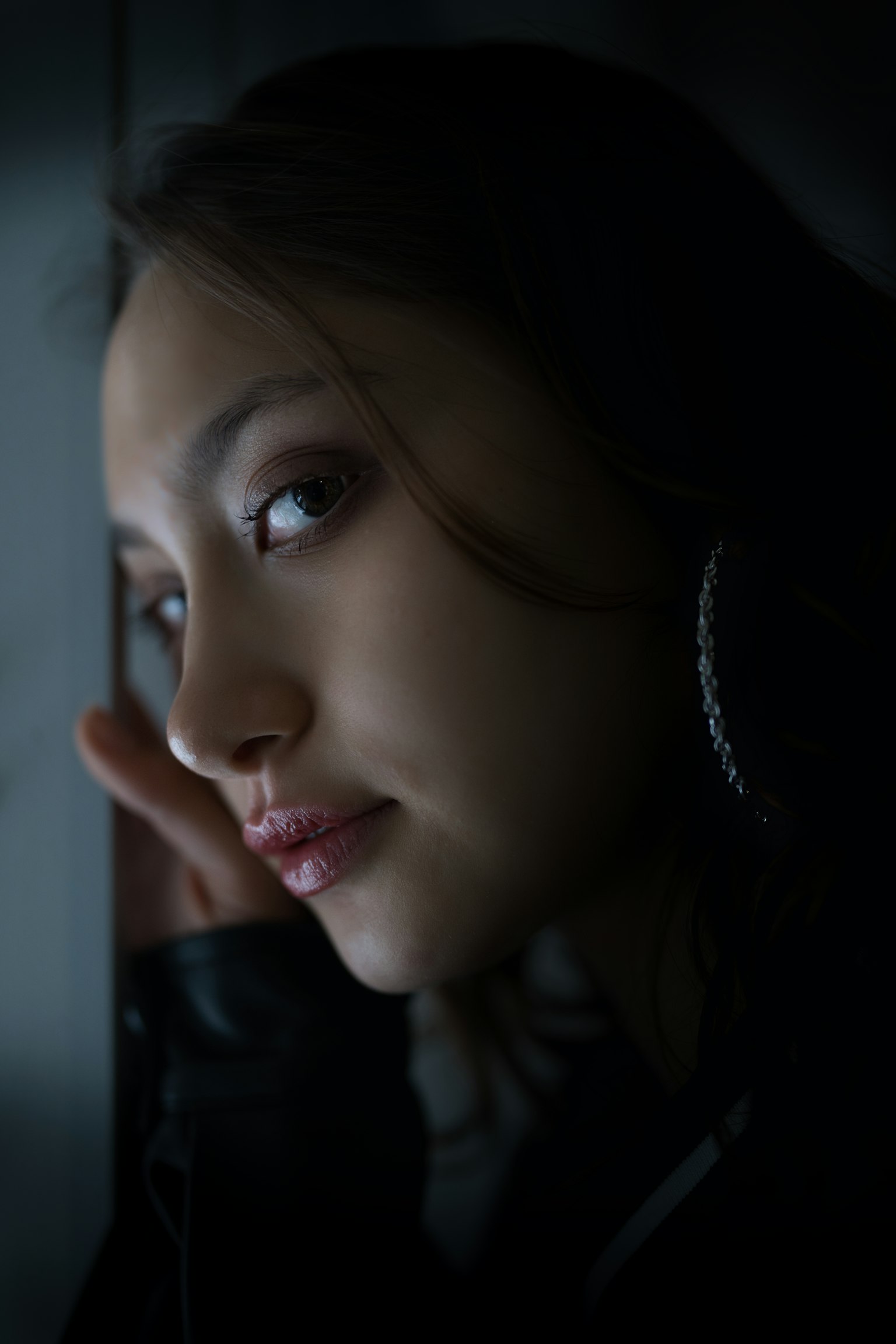 暗い背景に寄り添う女性の横顔 髪は長く滑らかで大きなイヤリングを着用