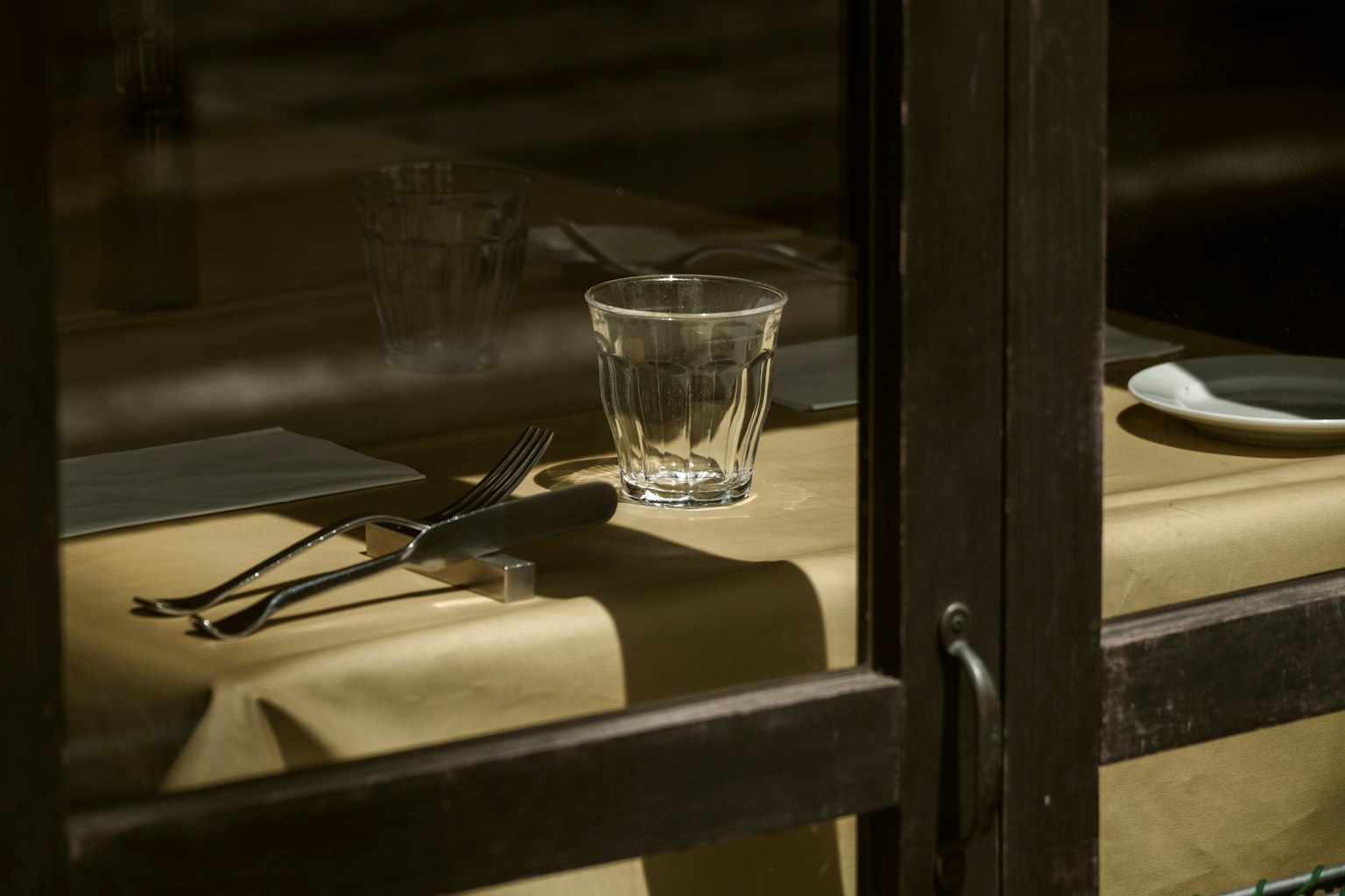 Acercamiento de un vaso y cubiertos sobre una mesa con un mantel beige