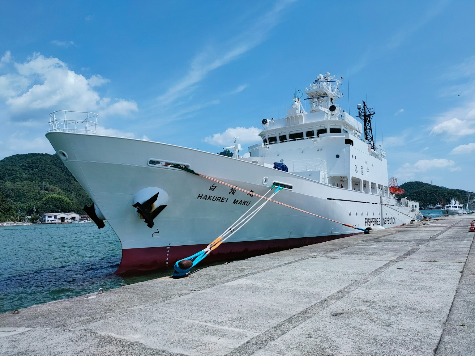 Large white research vessel docked at the port with blue sky and mountains in the background