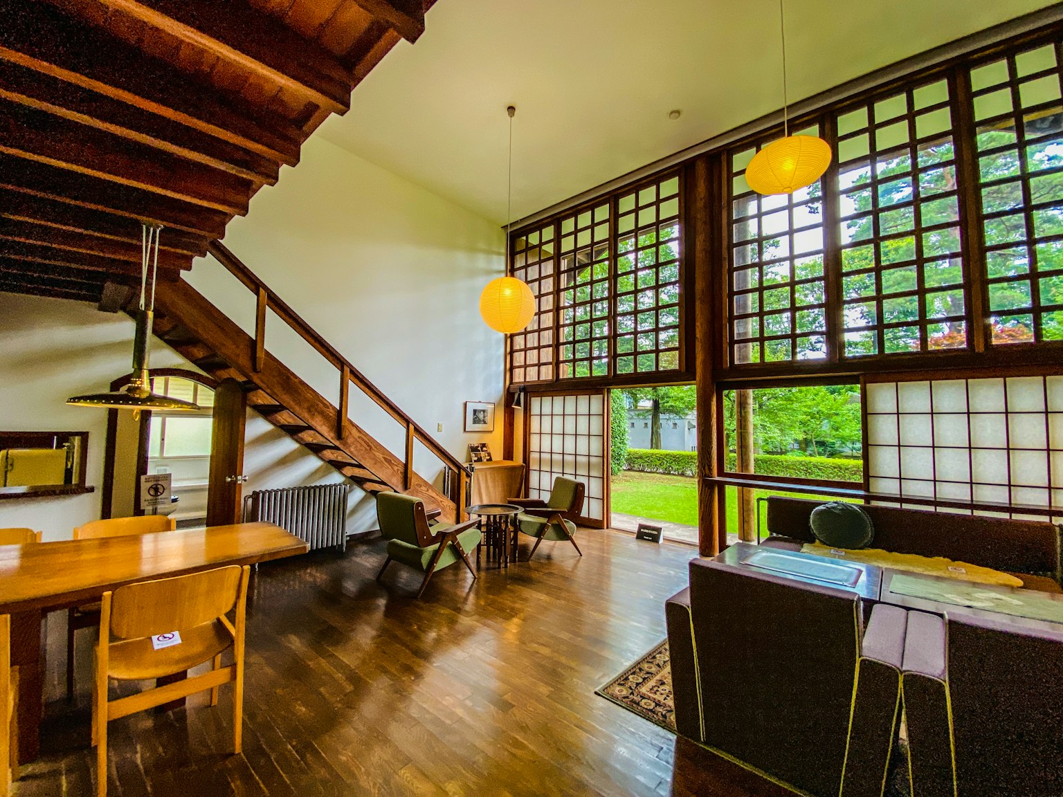 Geräumiges modernes Wohnzimmer mit Holztreppe große Fenster, die natürliches Licht und Ausblicke auf die grüne Umgebung bieten