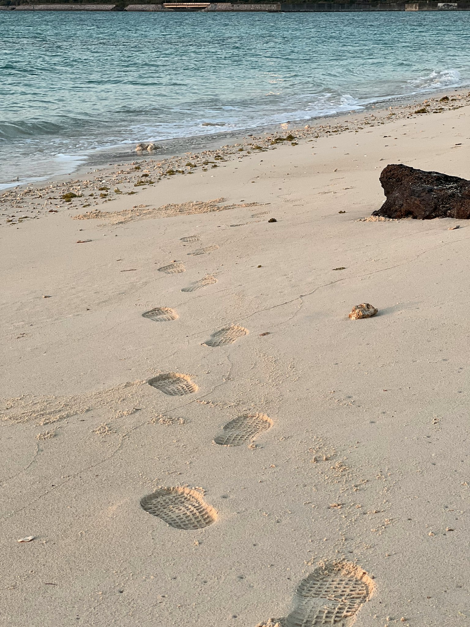 Jejak kaki di pantai berpasir dekat ombak dan batu