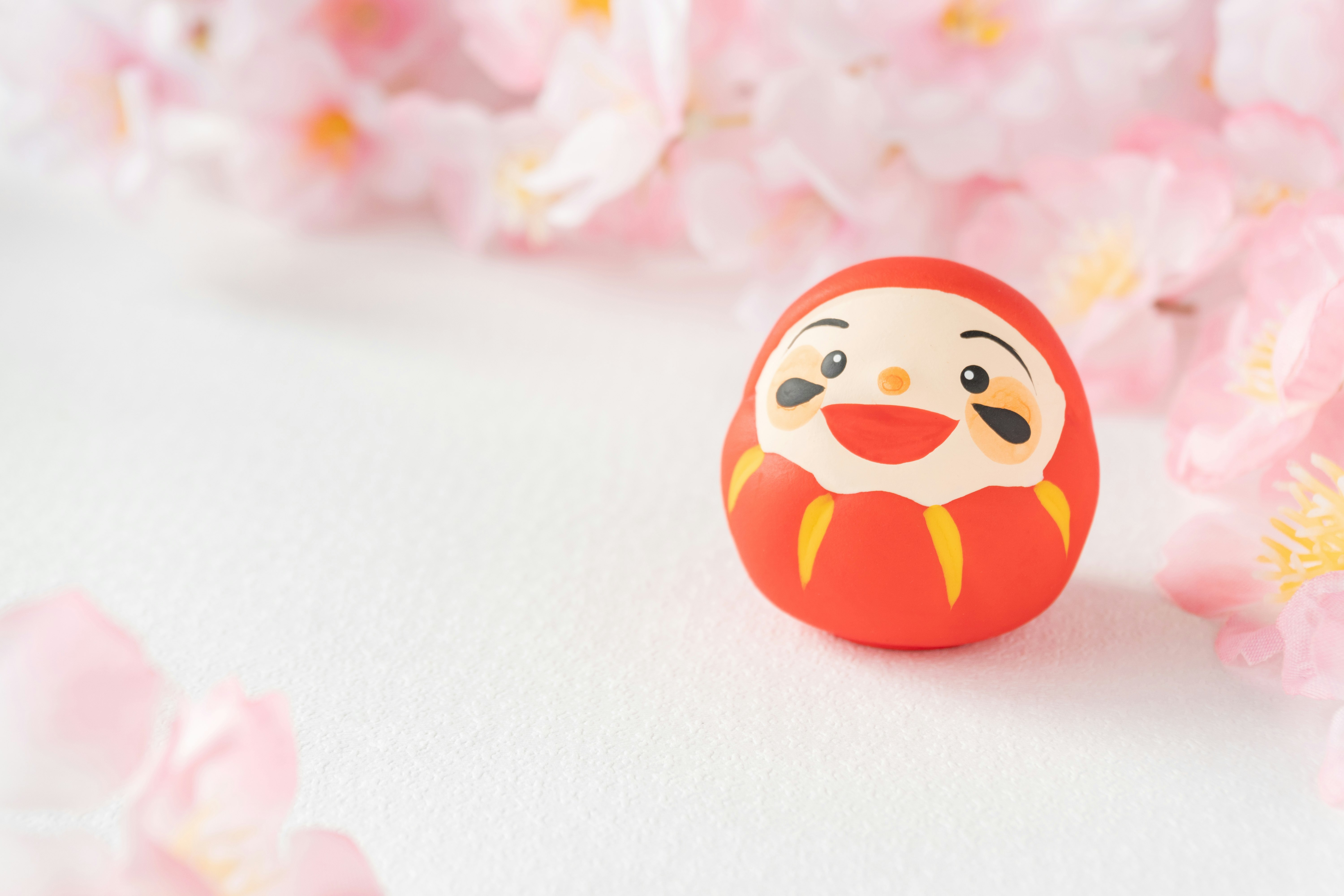 Daruma-style charm on a pink petal background