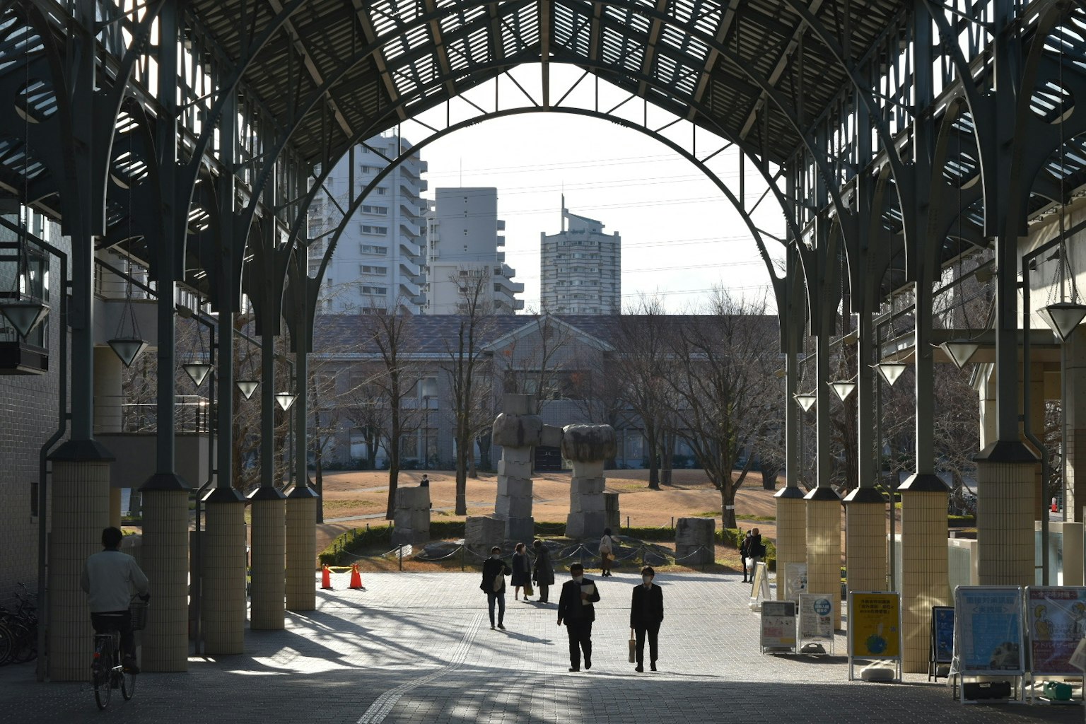 Personas caminando bajo un techo arqueado con edificios al fondo