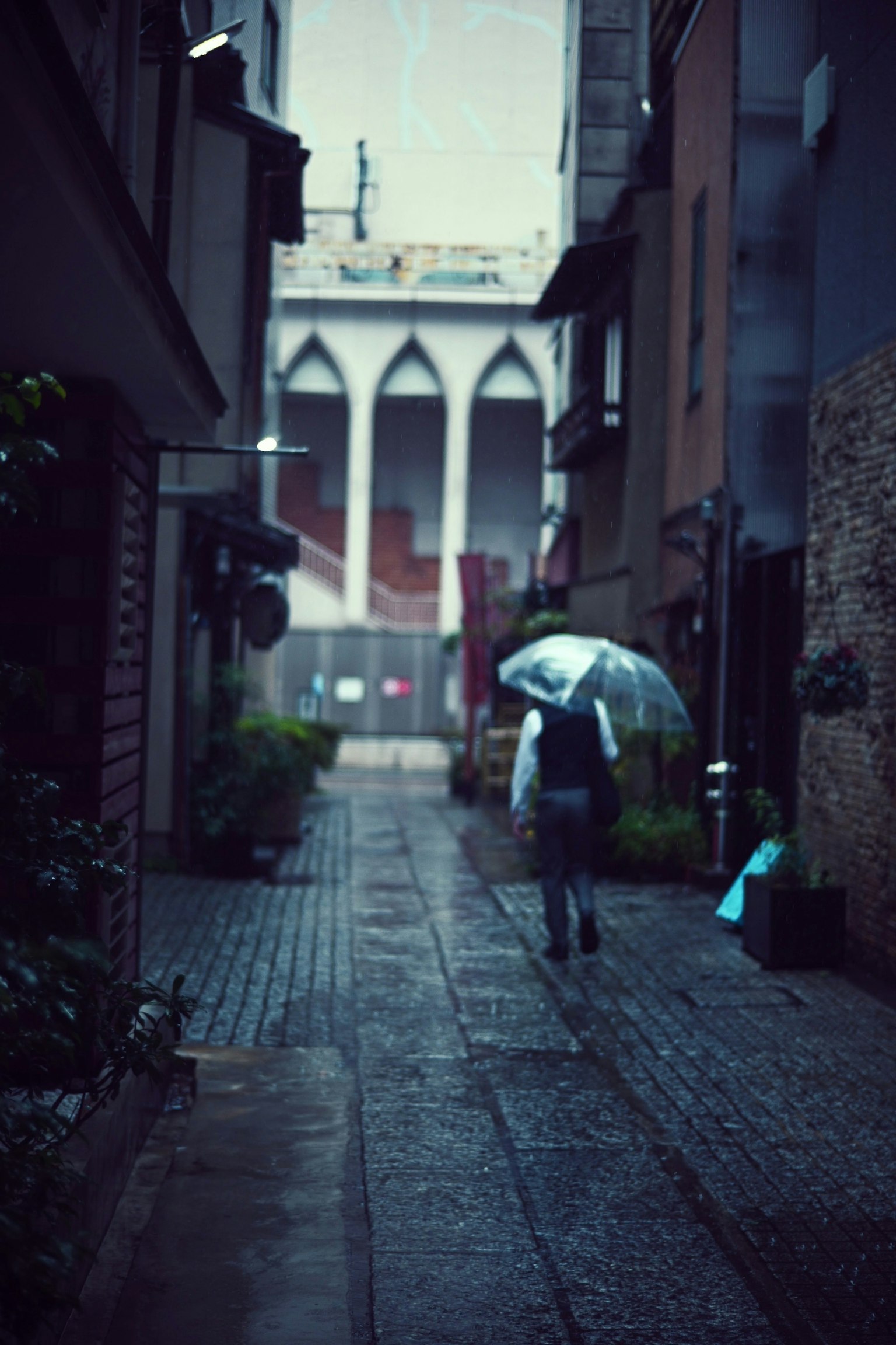Eine Person, die in einer engen Gasse mit einem Regenschirm im Regen geht, mit einem markanten Gebäude im Hintergrund