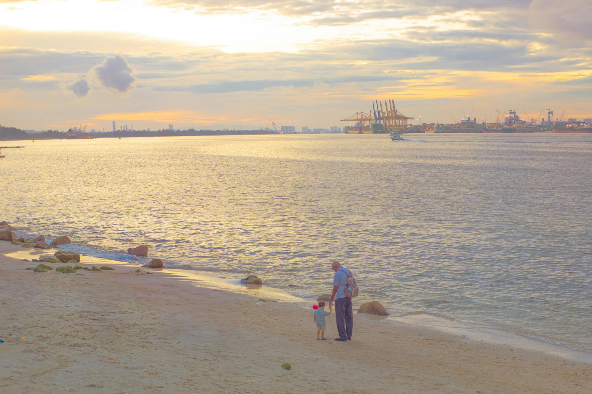 夕日を背景にした海岸で、老人と子供が立っている風景