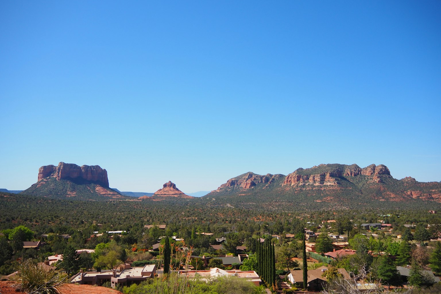 Vista escénica de las formaciones rocosas rojas de Sedona bajo un cielo azul claro con árboles verdes y casas