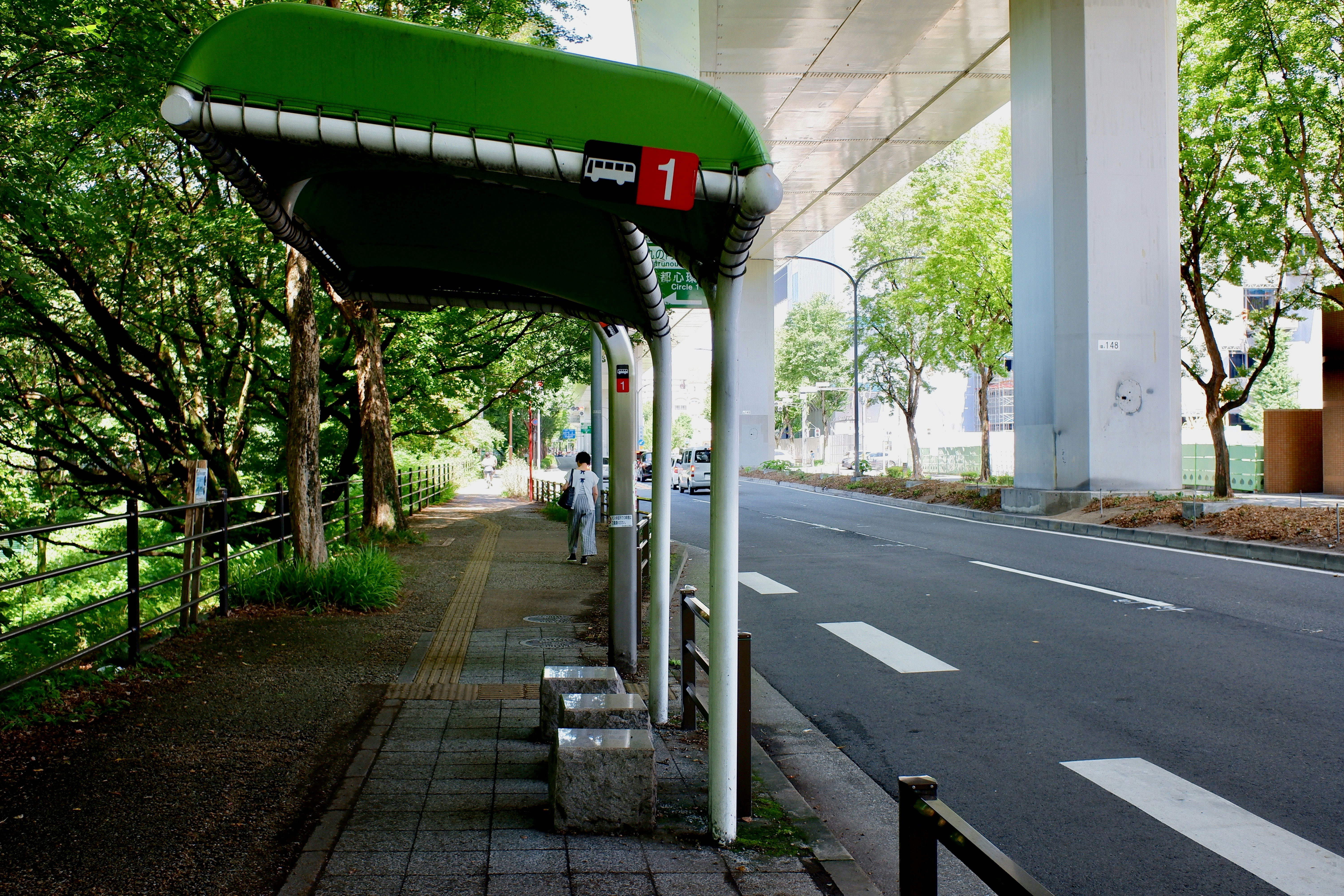 acera junto a una calle con marquesina verde de parada de autobús y árboles
