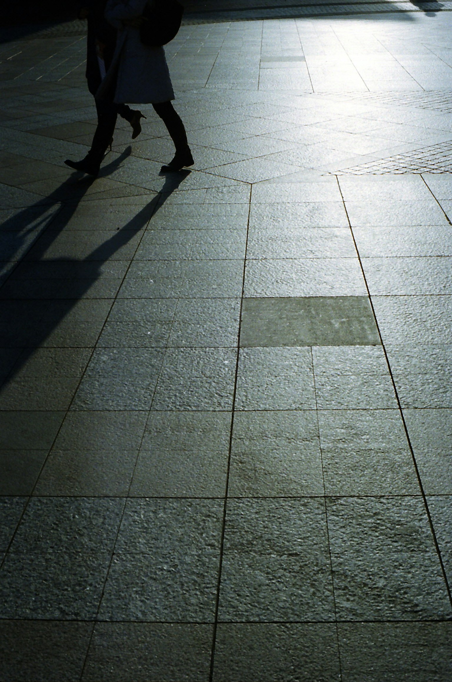 Pieds de personnes marchant sur un pavé ensoleillé avec des ombres