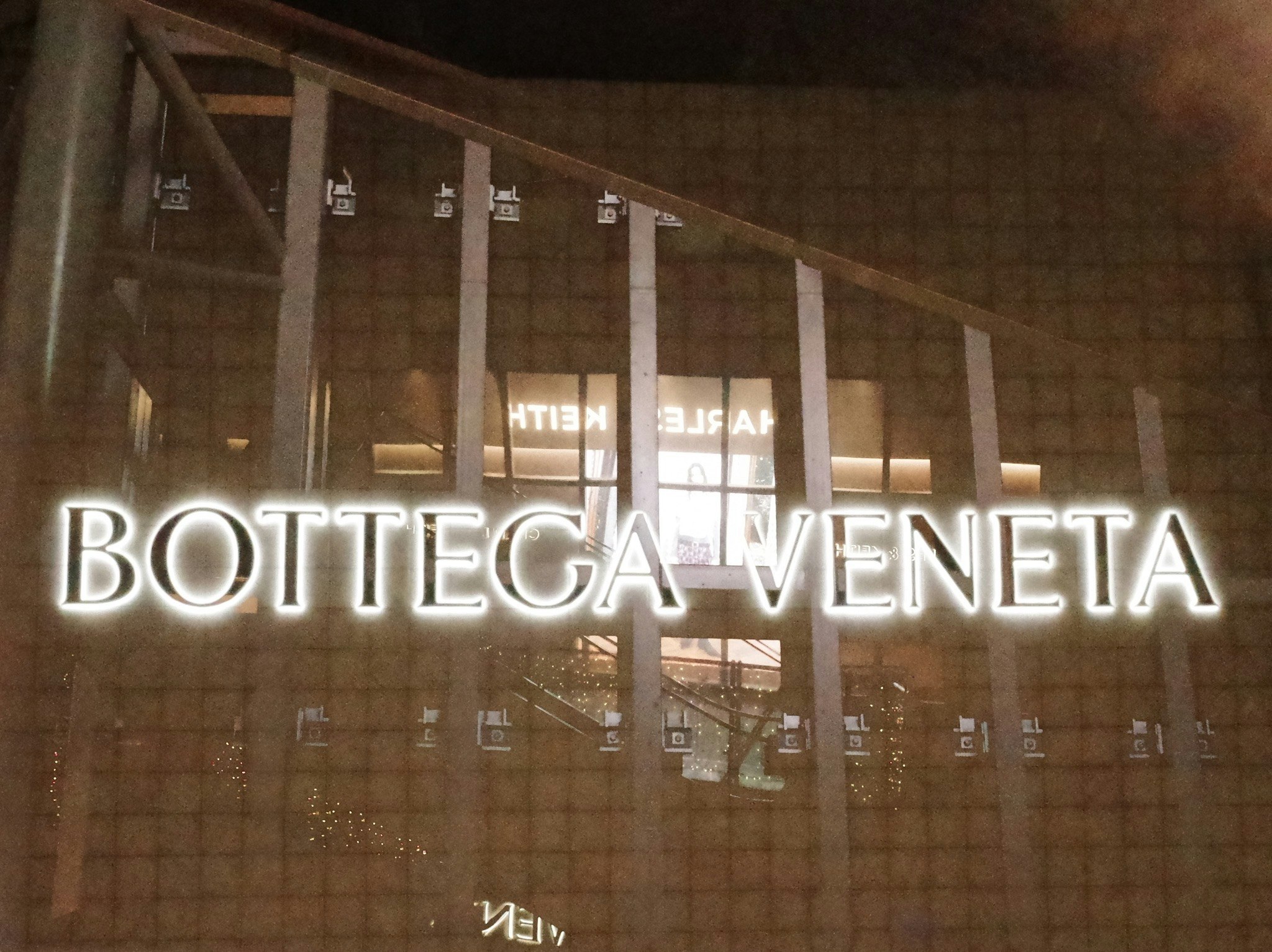 ガラス越しの壁面に映る「BOTTEGA VENETA」ネオン文字のディスプレイ
