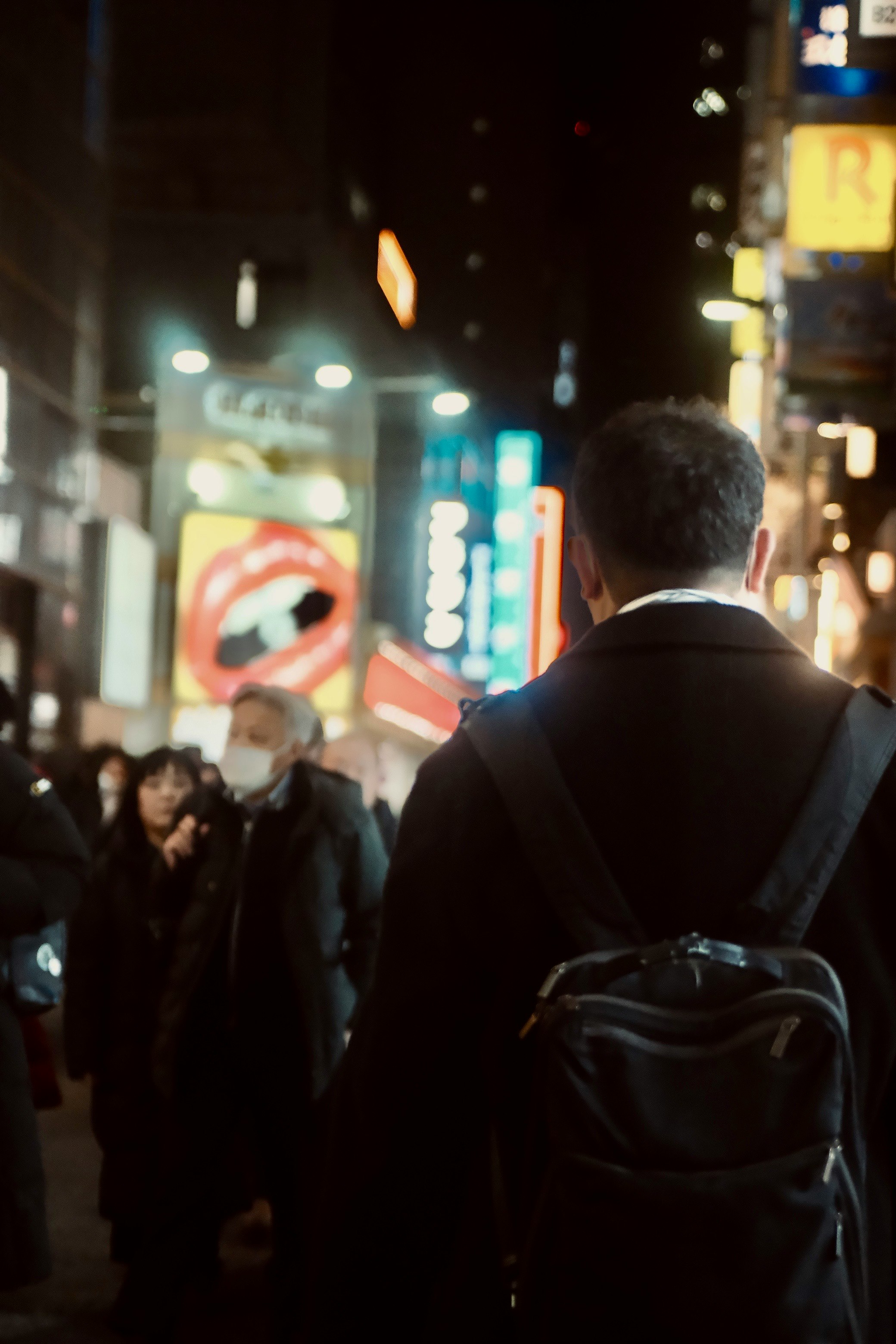 夜の繁華街で背中を向けて歩く人と街灯の光