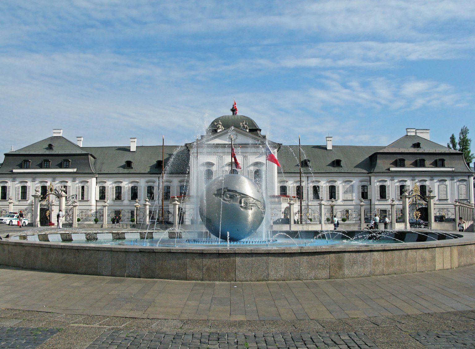 A spherical sculpture in a fountain with a historic white building in the background