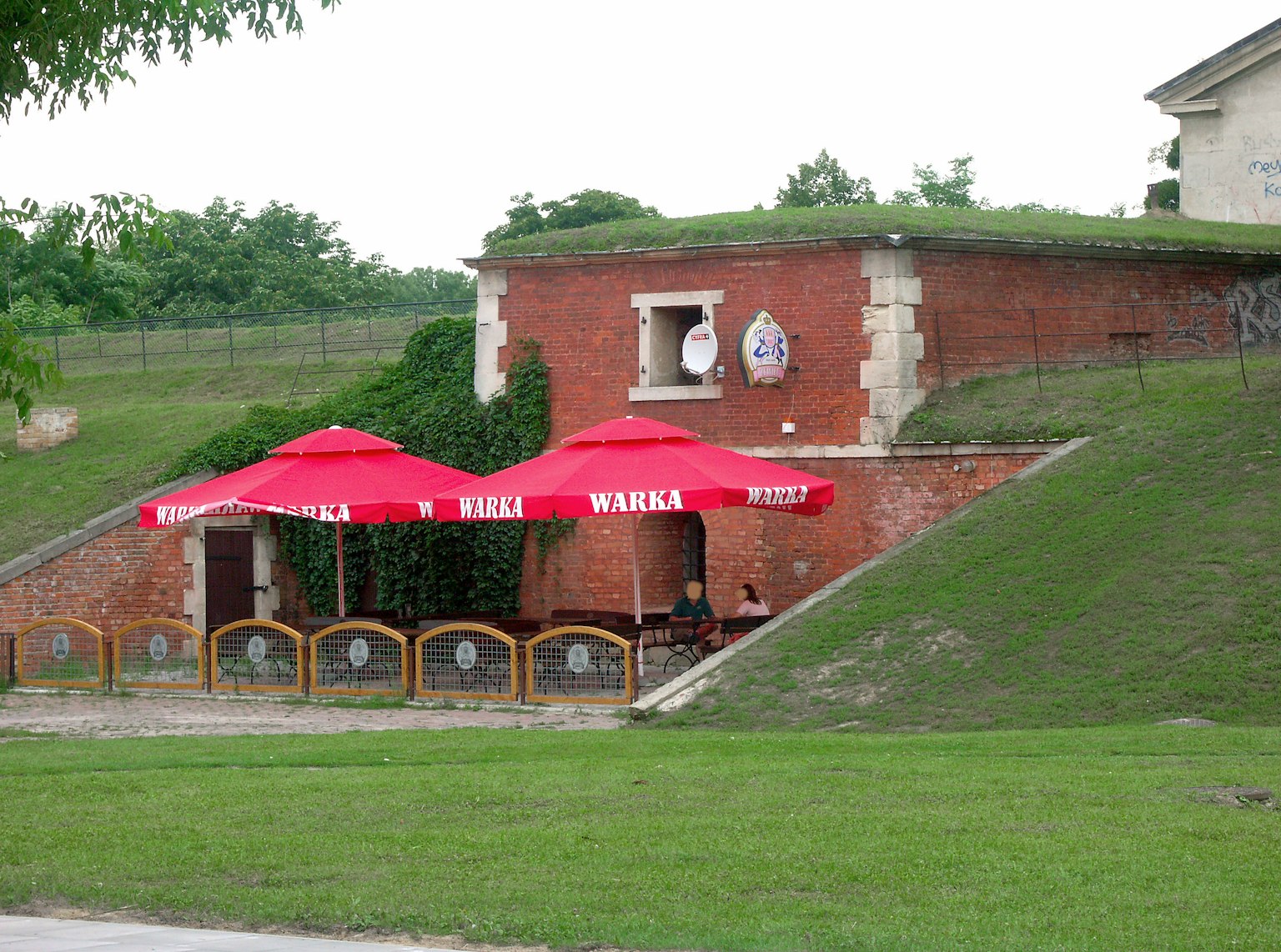 ภายนอกของร้านอาหารที่มีร่มสีแดงและเนินเขาสีเขียว