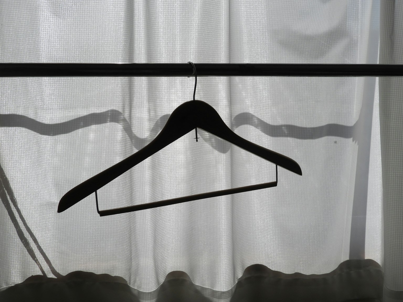 Black hanger suspended behind white curtain