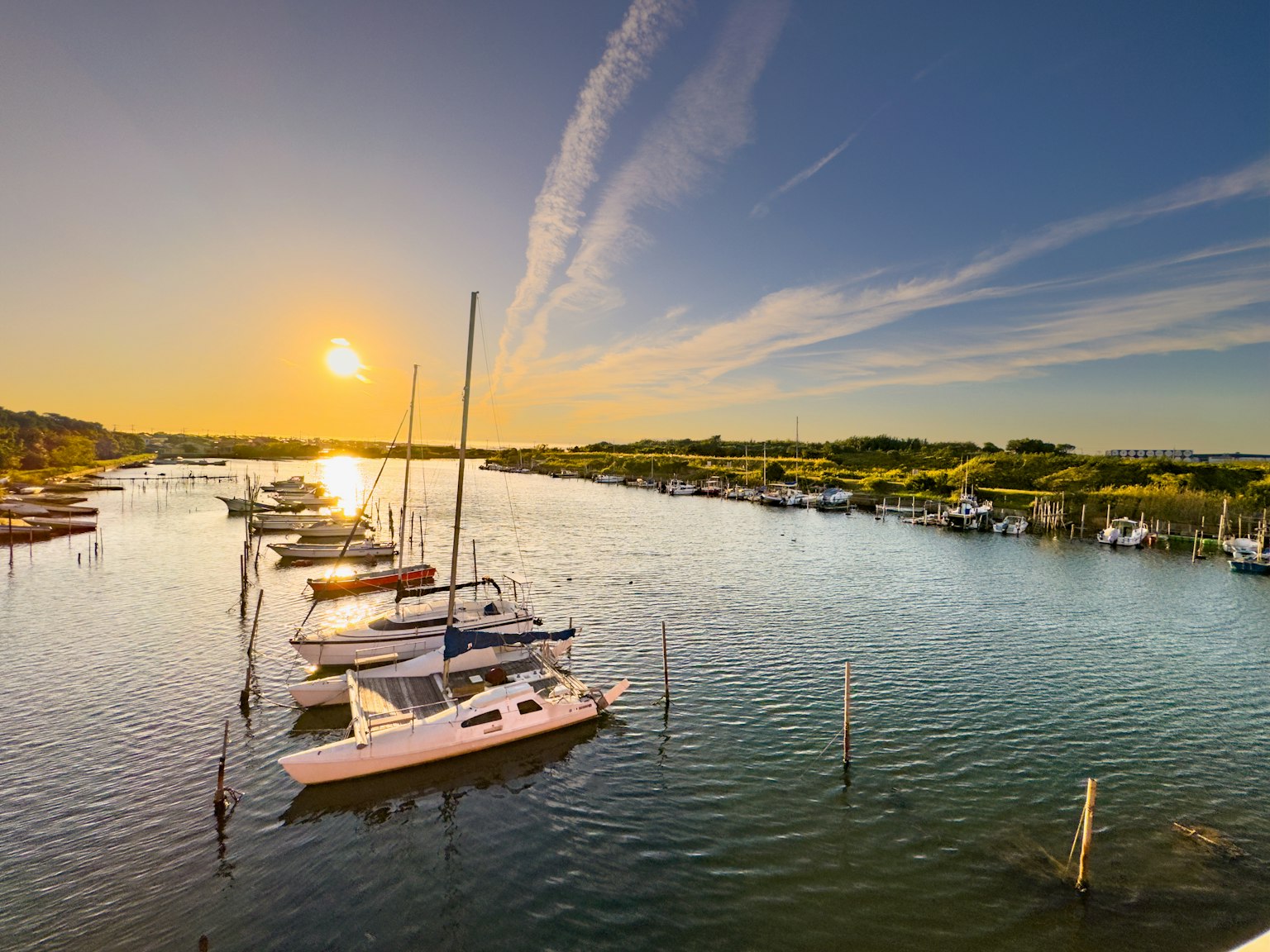 A serene river landscape with moored yachts and boats under a sunset