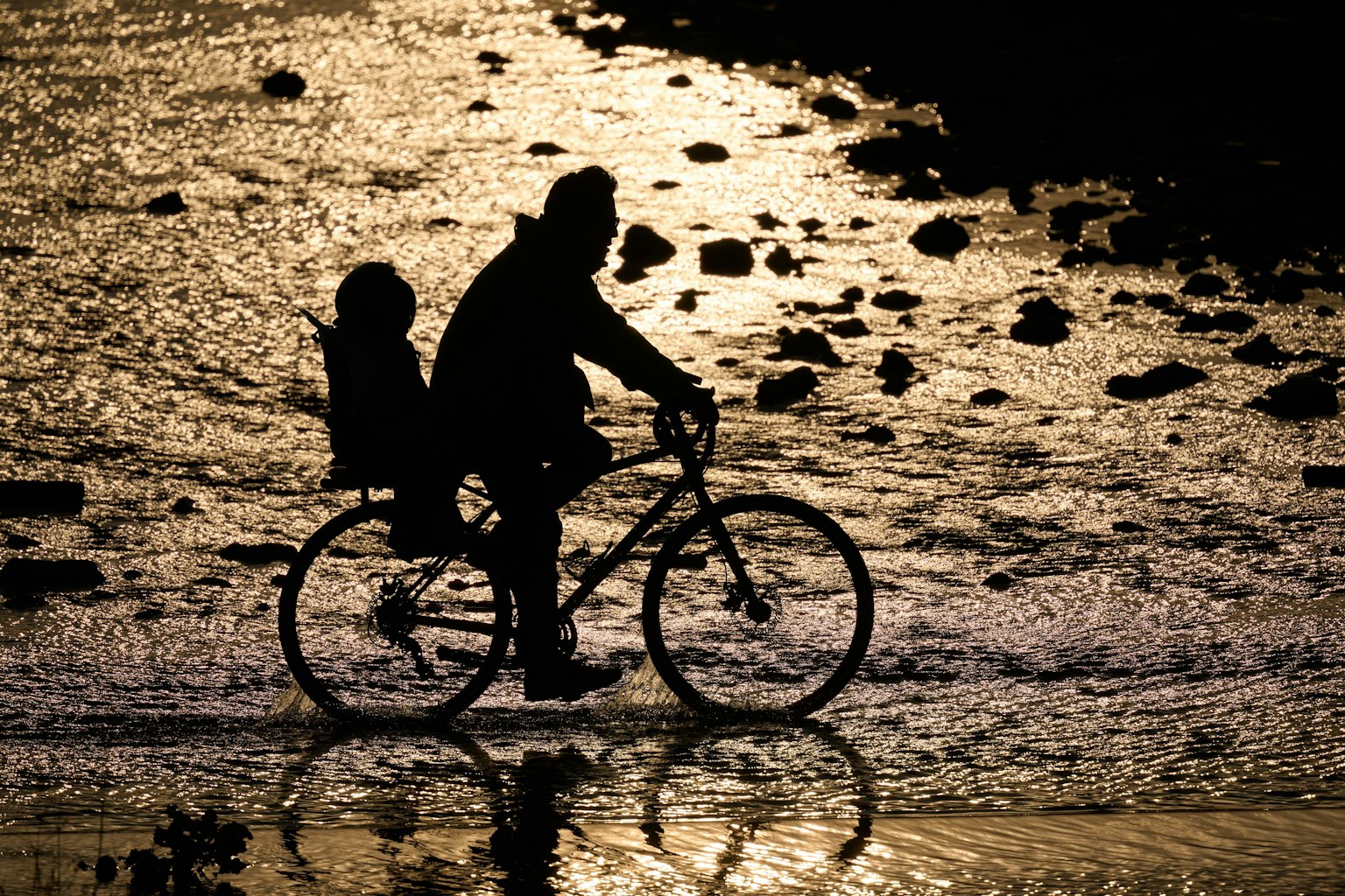 Silhouette d'une personne faisant du vélo avec un enfant sur la plage au coucher du soleil