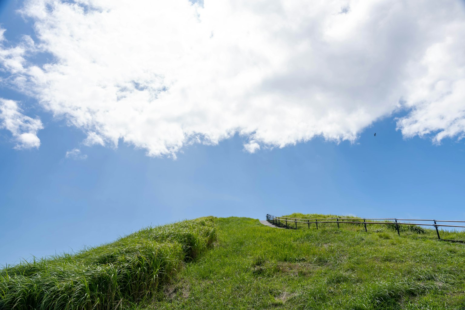 Bukit hijau dikelilingi langit biru dan awan putih